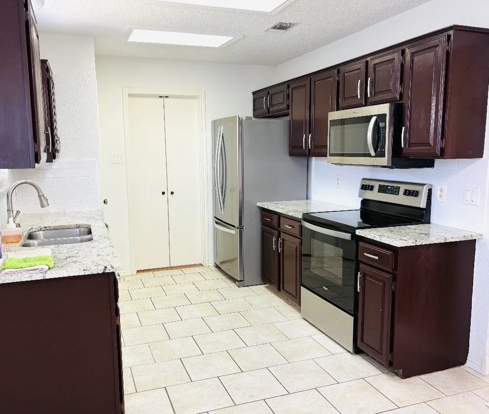 Kitchen featuring dark wood cabinetry, granite countertops, subway tile backsplash, and stainless steel appliances