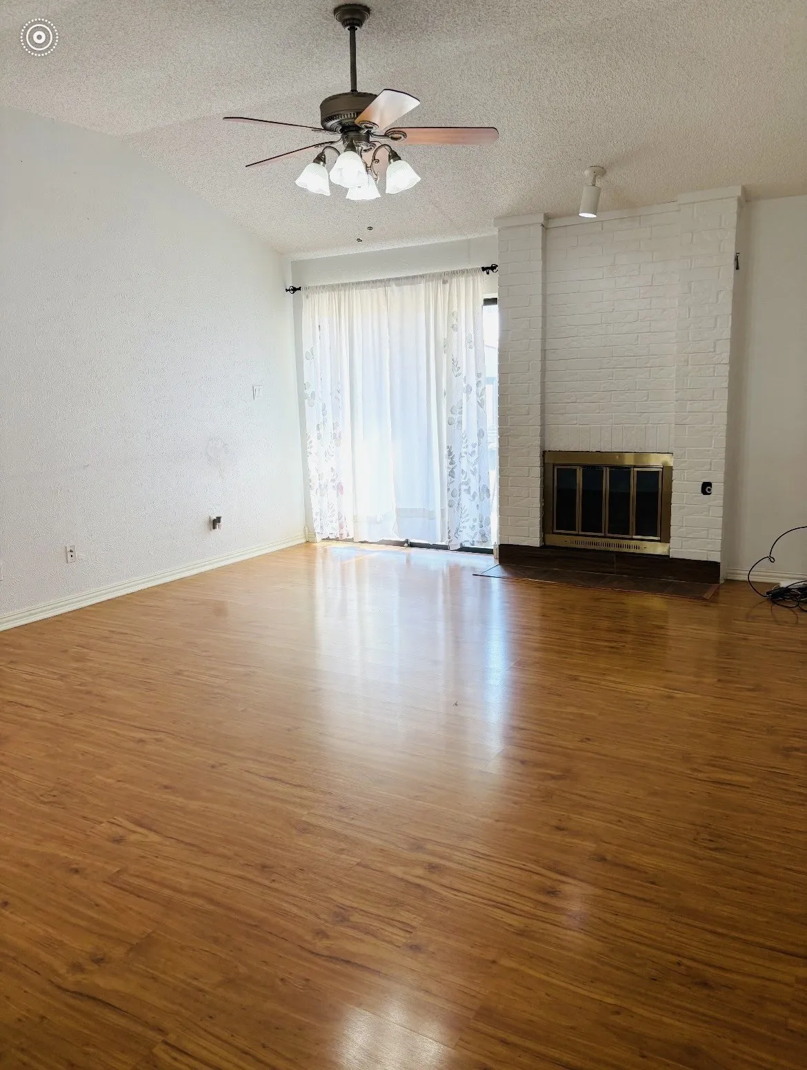 Vaulted ceiling with a ceiling fan light fixture, wood-finish flooring, white painted brick fireplace, and sliding glass doors