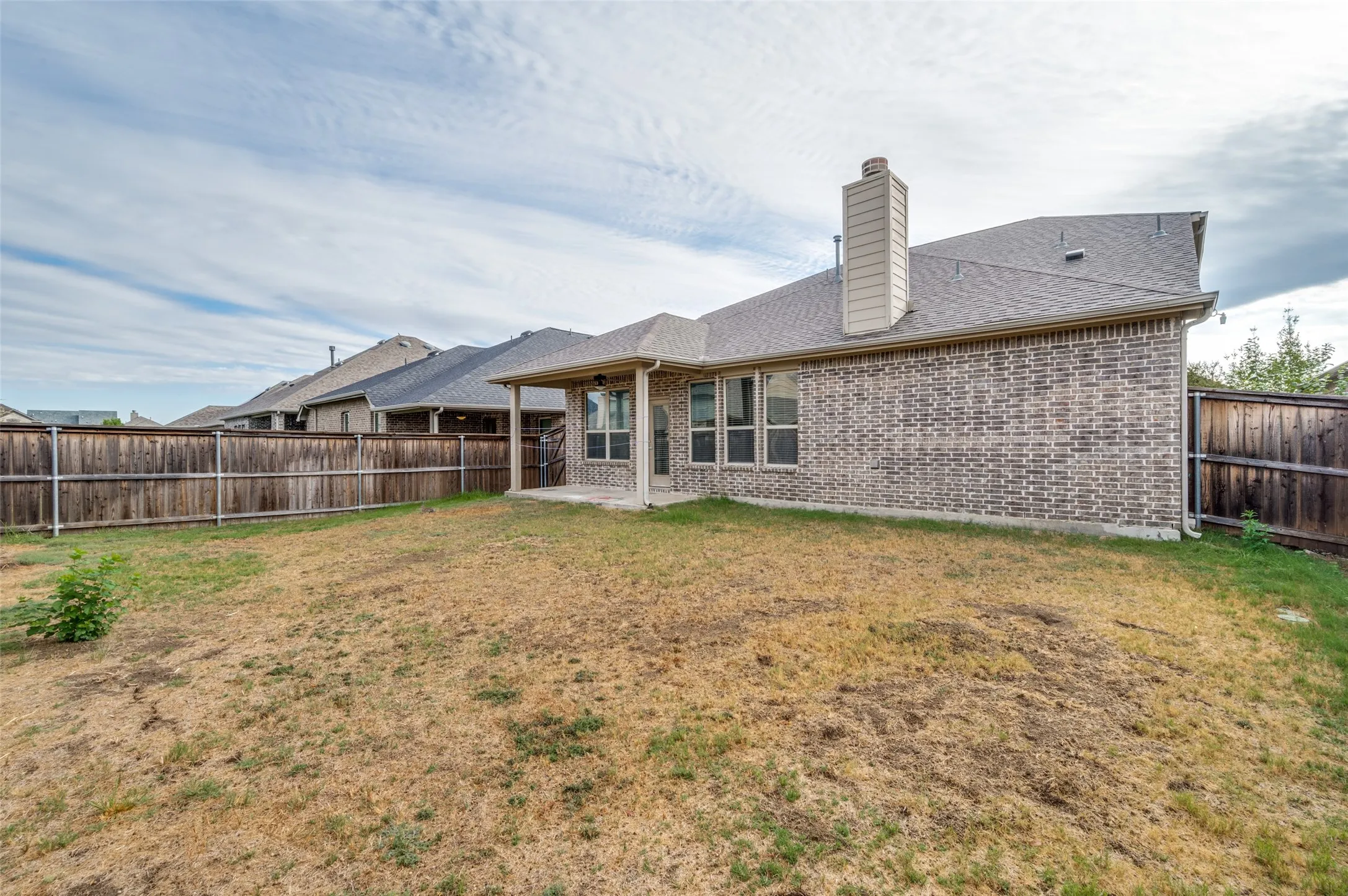 Expansive backyard with a full privacy fence, covered patio, brick exterior, and a built-in chimney