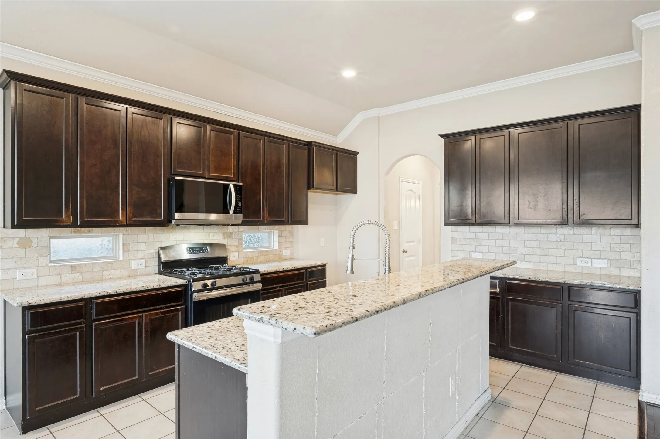 Kitchen featuring dark wood-finish cabinetry, light-toned granite countertops, a tiled backsplash, a built-in microwave, and recessed lighting