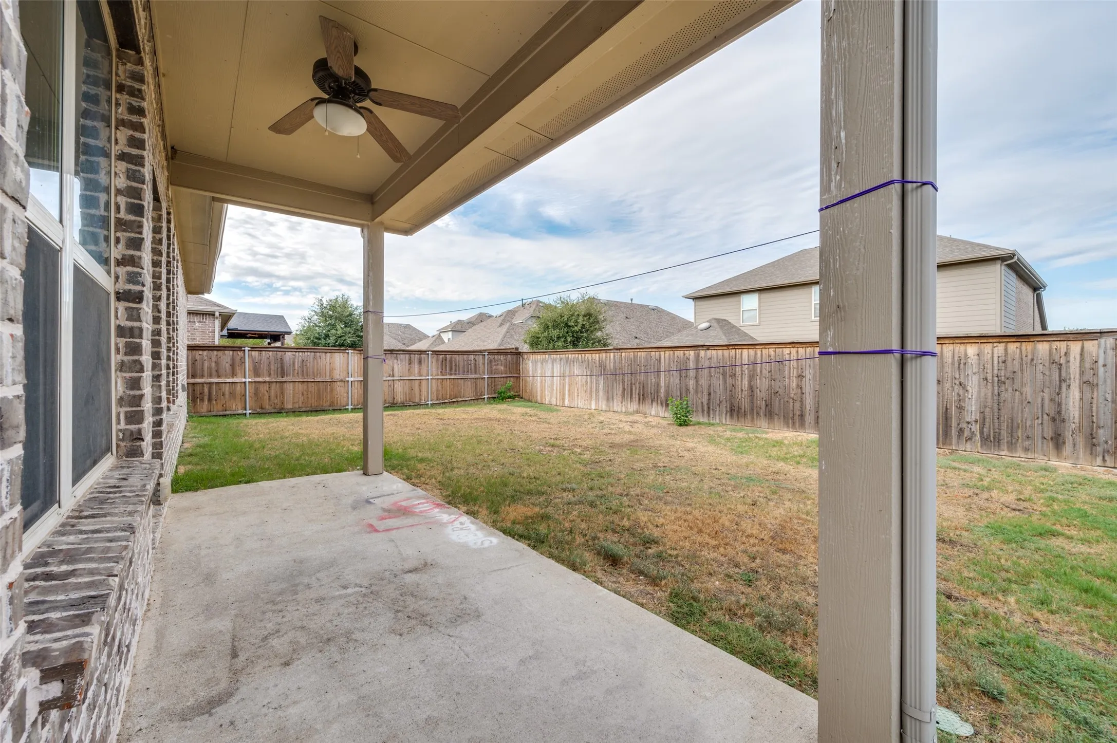 Covered concrete patio with ceiling fan, brick exterior, and fenced backyard
