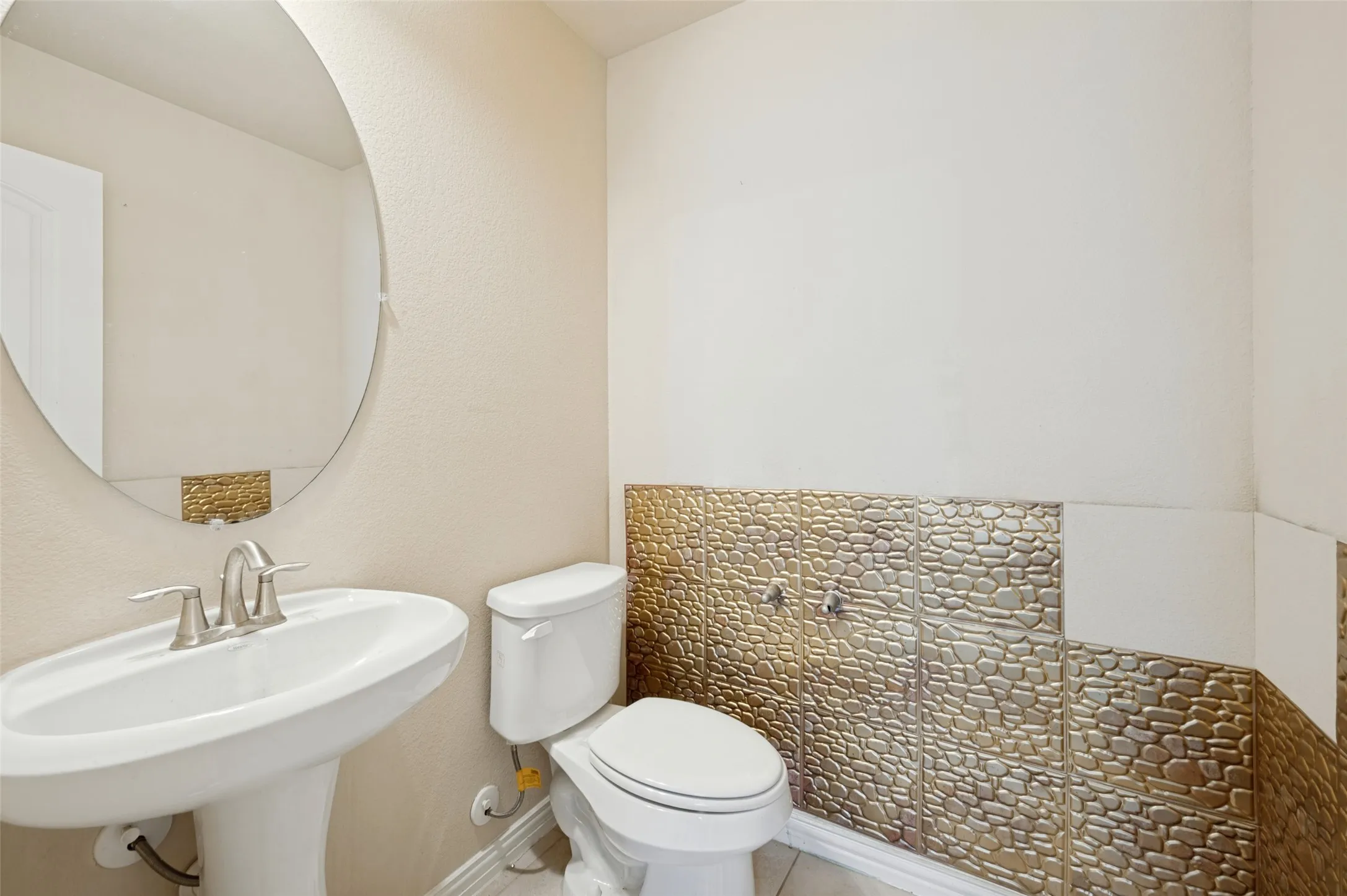 Pedestal sink with a polished chrome faucet, oval mirror, and decorative wall tiling