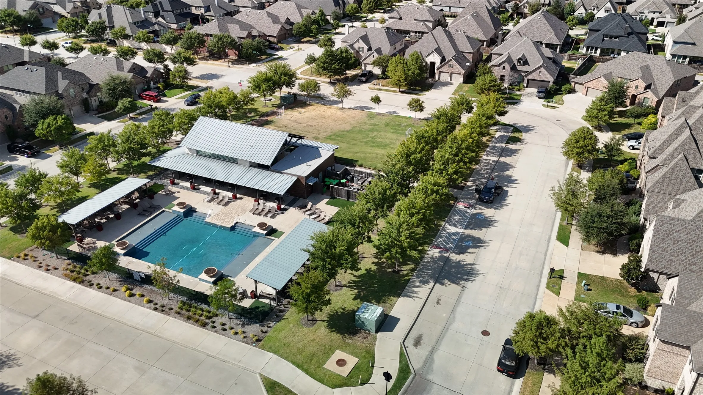 Community pool with surrounding patio, covered lounge areas, and expansive green space