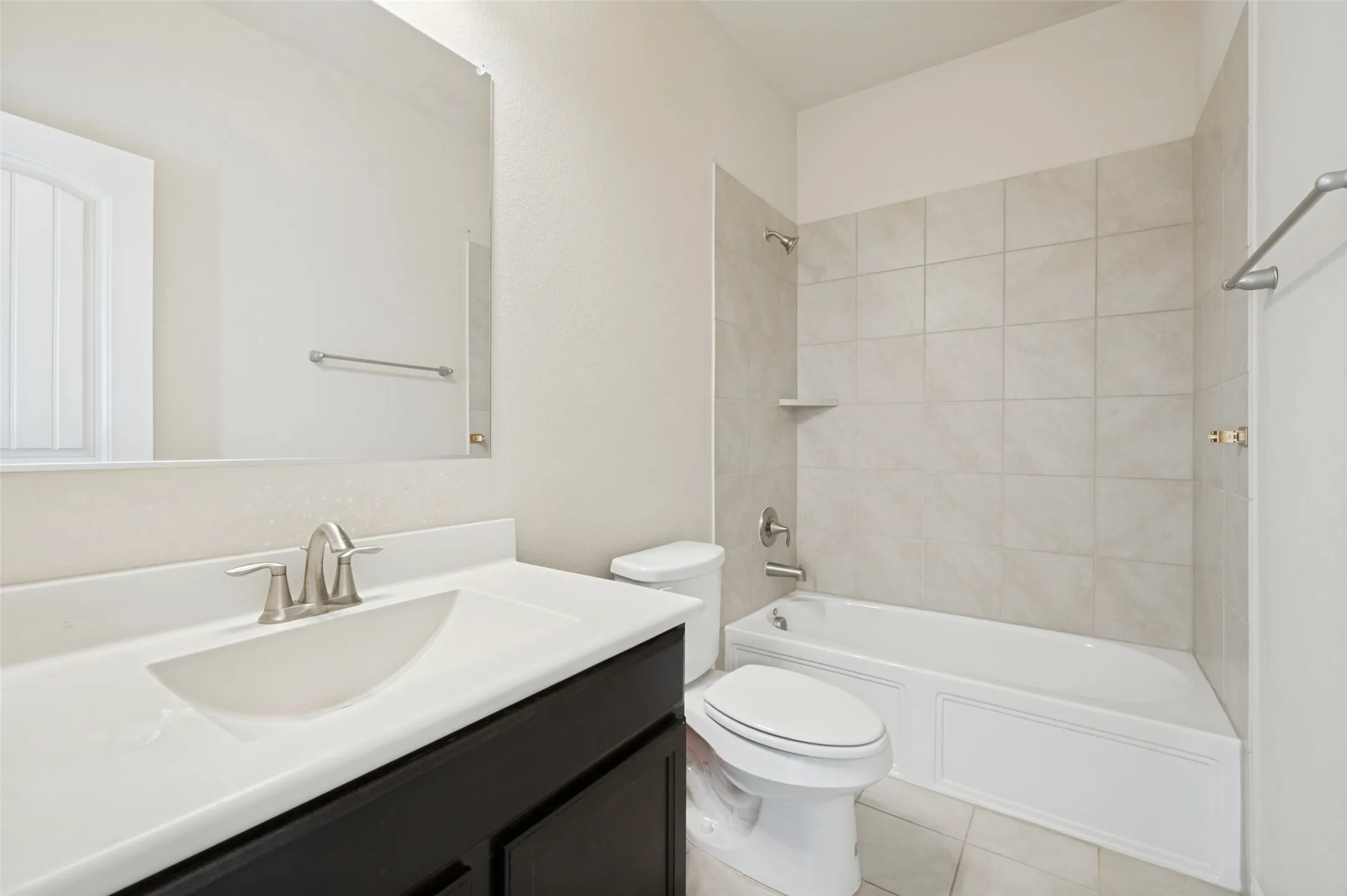 Bathroom featuring a dark wood-finish vanity with an integrated sink, brushed nickel faucet, and an undermount tub with subway tile surround