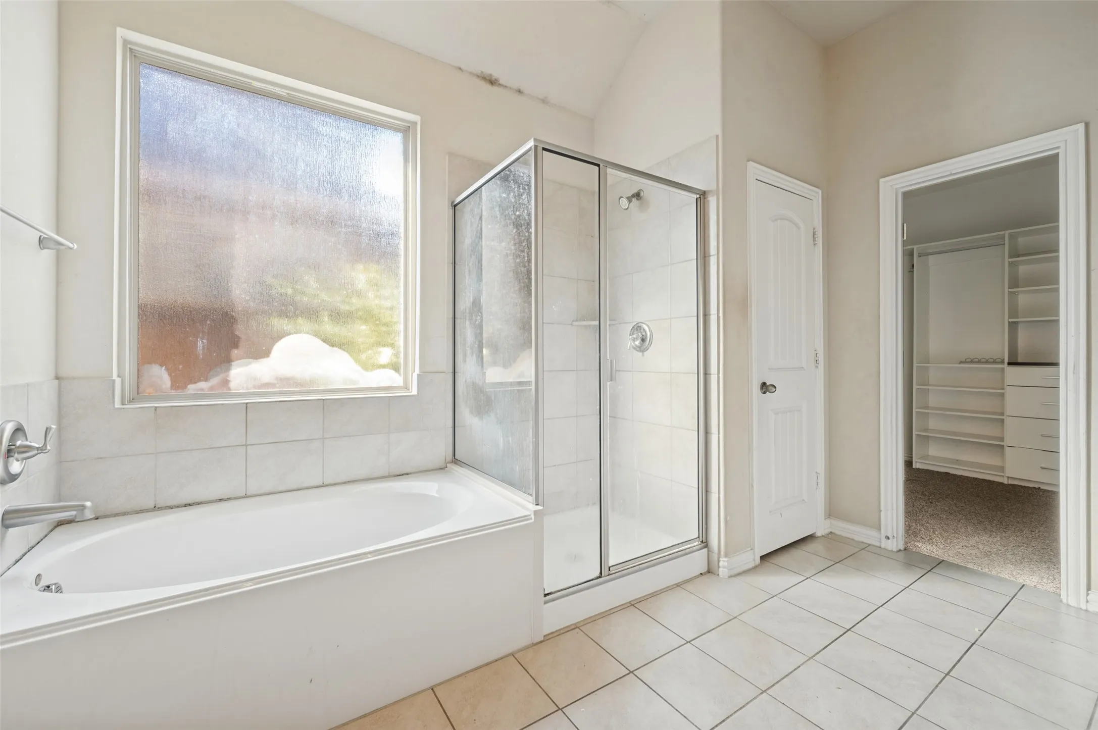 White tile flooring, built-in bathtub, glass-enclosed shower, and a separate water closet