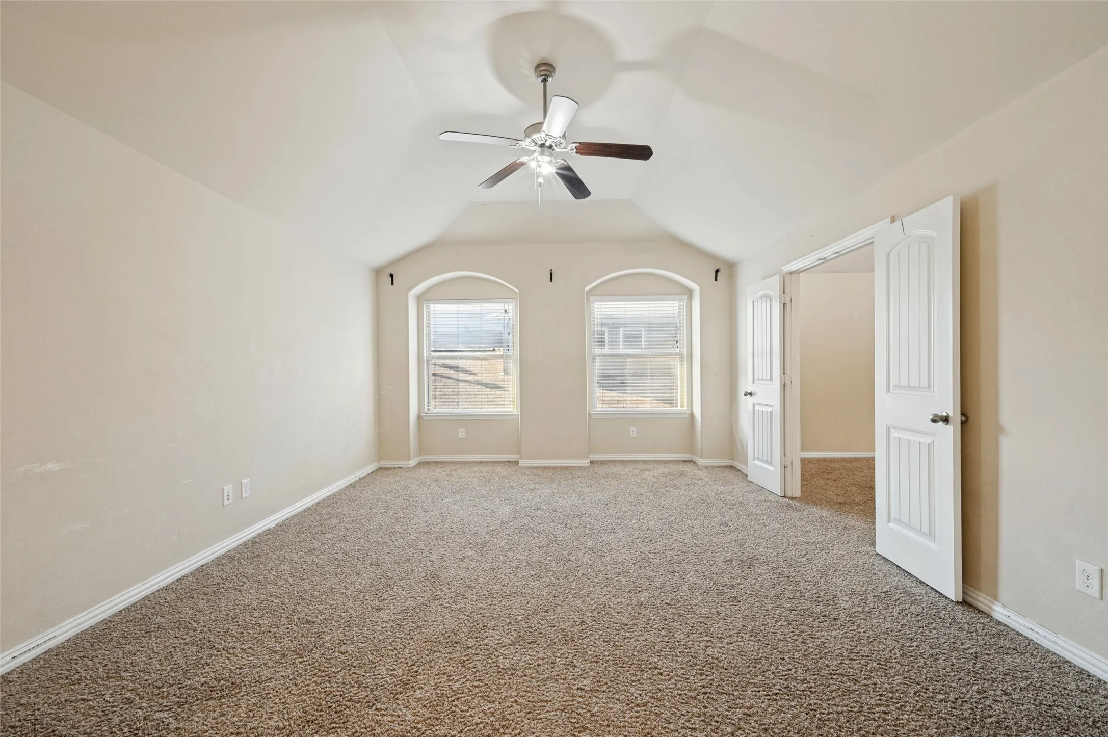 Vaulted ceiling with an attached ceiling fan, dual arched windows, and soft carpet flooring