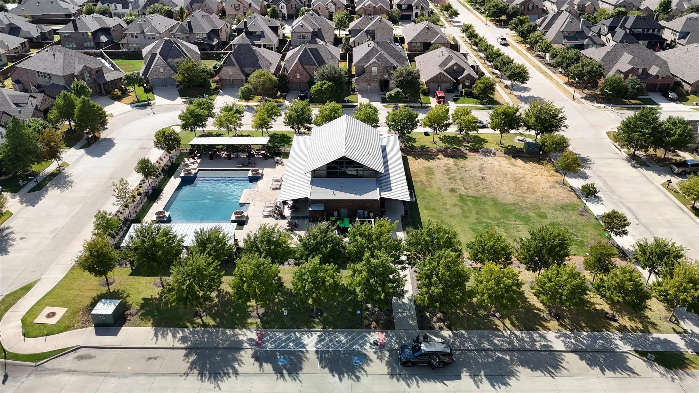 Community amenity center featuring a rectangular swimming pool, adjacent building with an A-frame roof, and open green space
