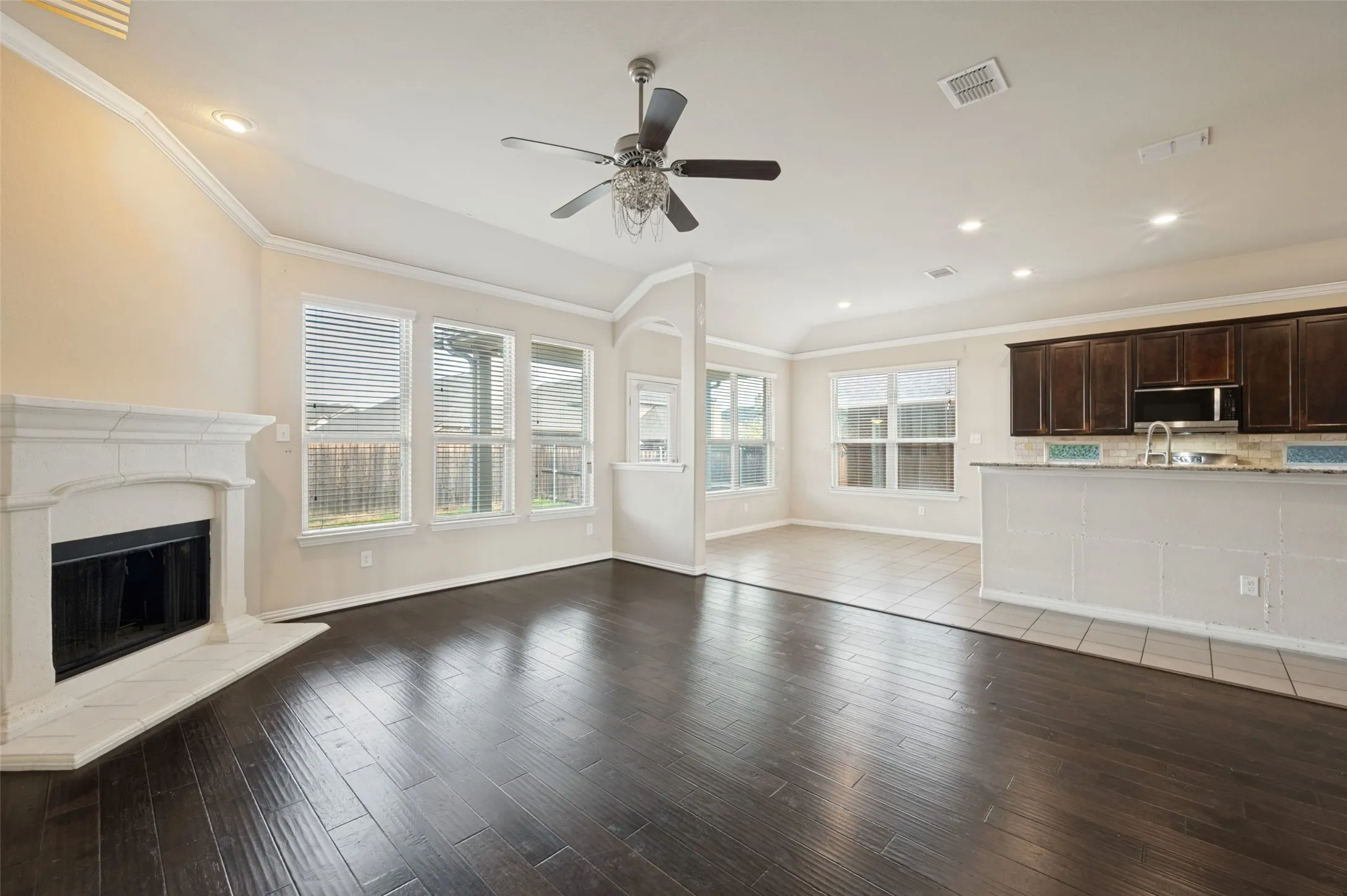 Wood-finish flooring, white mantel fireplace, recessed lighting, ceiling fan with light fixture, and dark wood cabinetry with integrated appliances