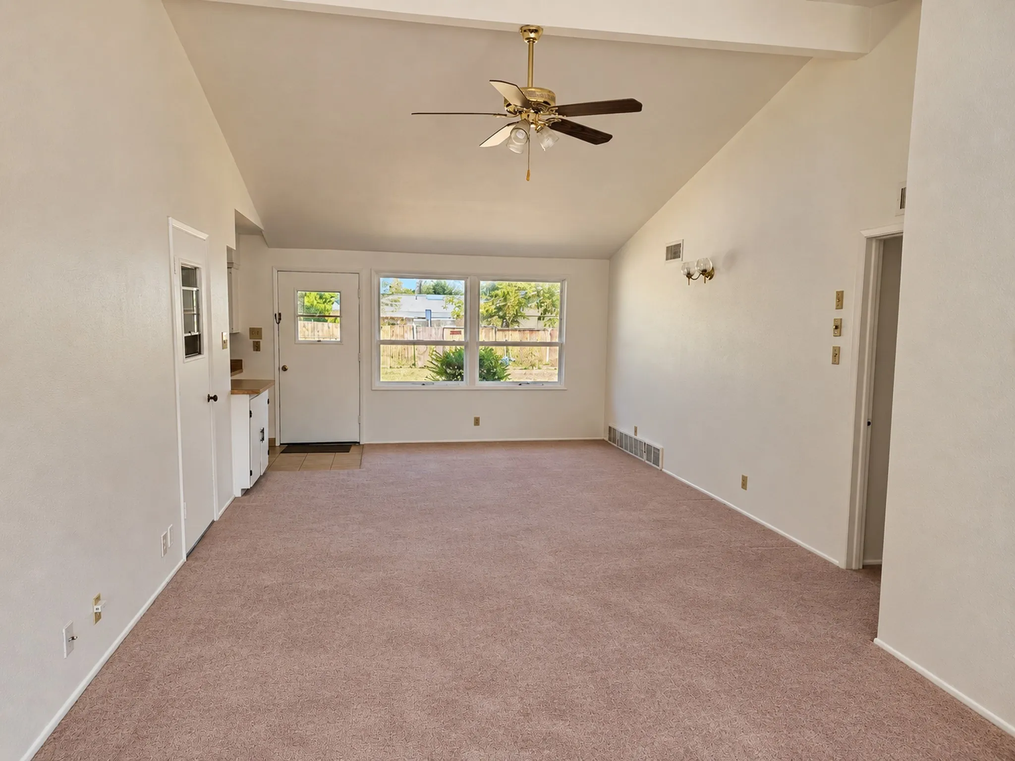 Vaulted ceilings with exposed beam, multiple windows, ceiling fan, and sconce lighting