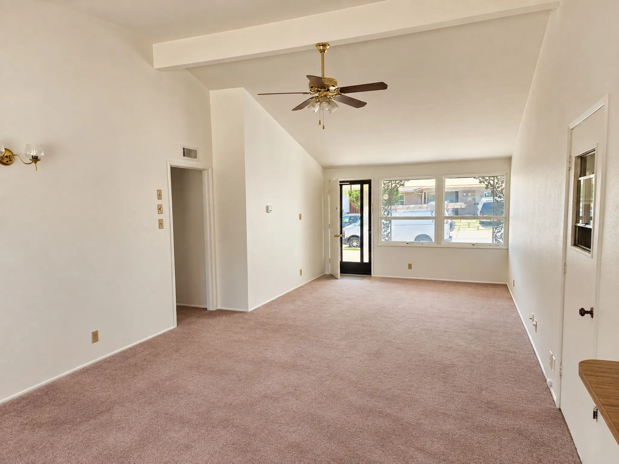 Vaulted ceiling with exposed beam, ceiling fan, carpet flooring, and front-facing windows