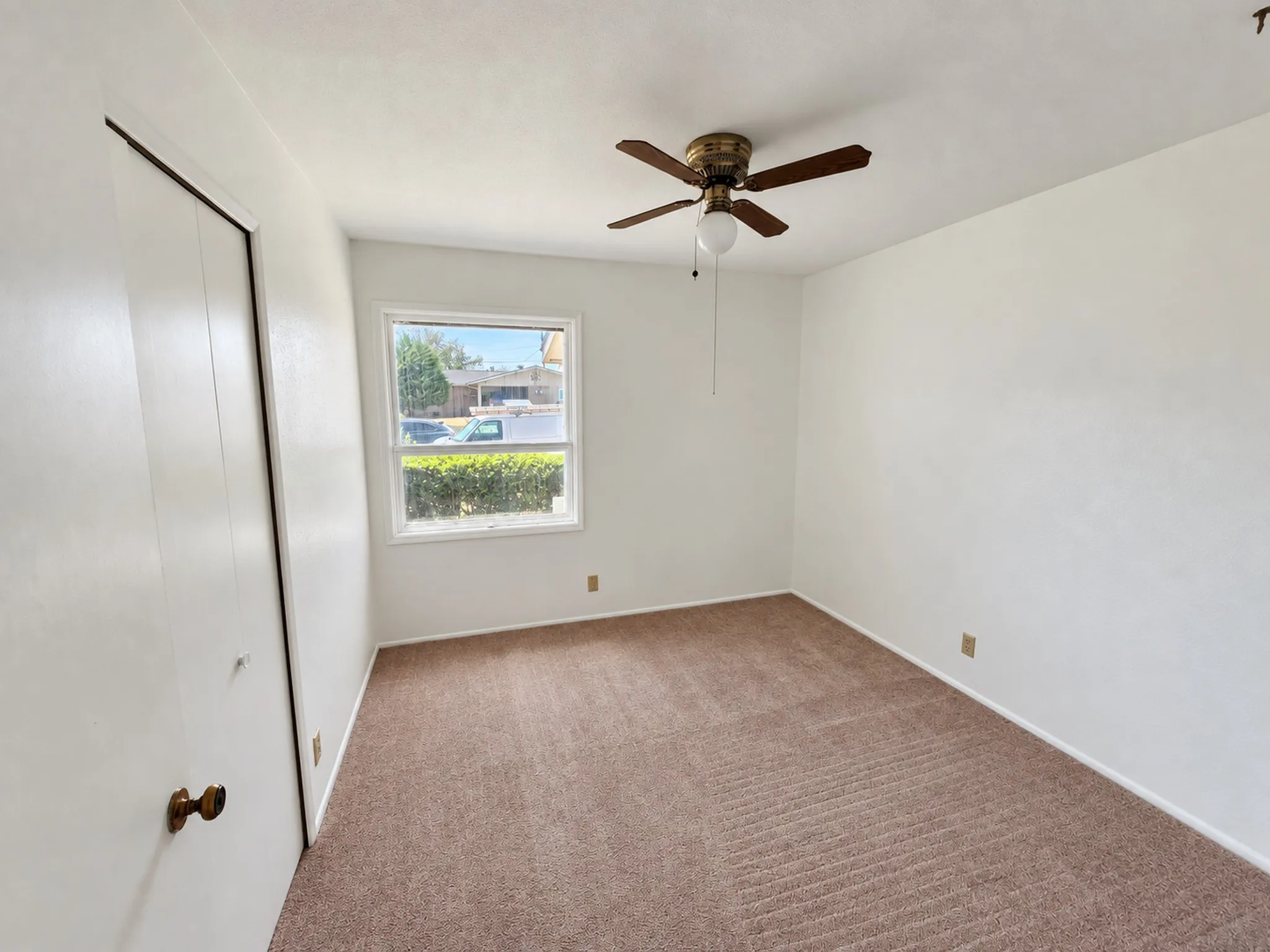 Neutral wall finishes, carpet flooring, a window with exterior visibility, a ceiling fan, and bi-fold closet doors