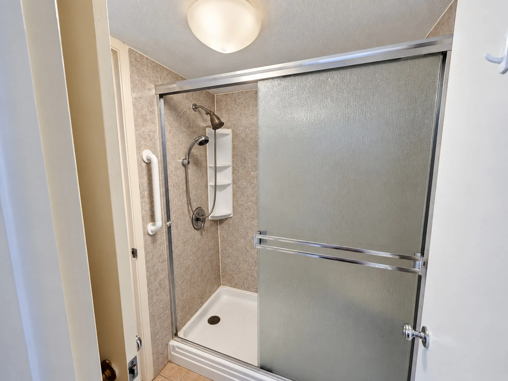 Walk-in shower with textured sliding glass doors, built-in shelving, and a mounted grab bar