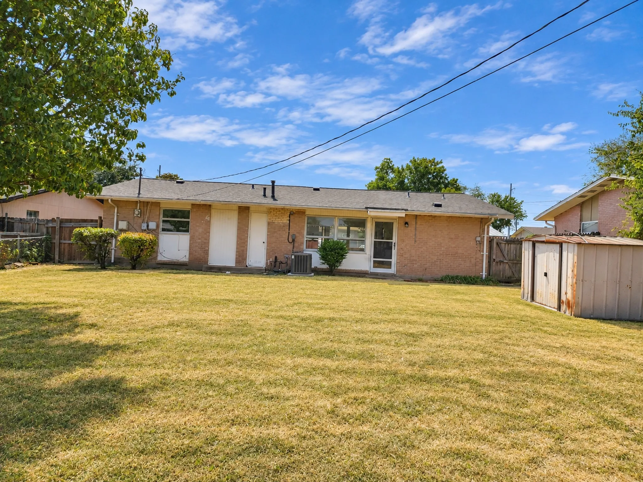 Expansive grass lawn with a storage shed, a partial wood fence, and mature foliage