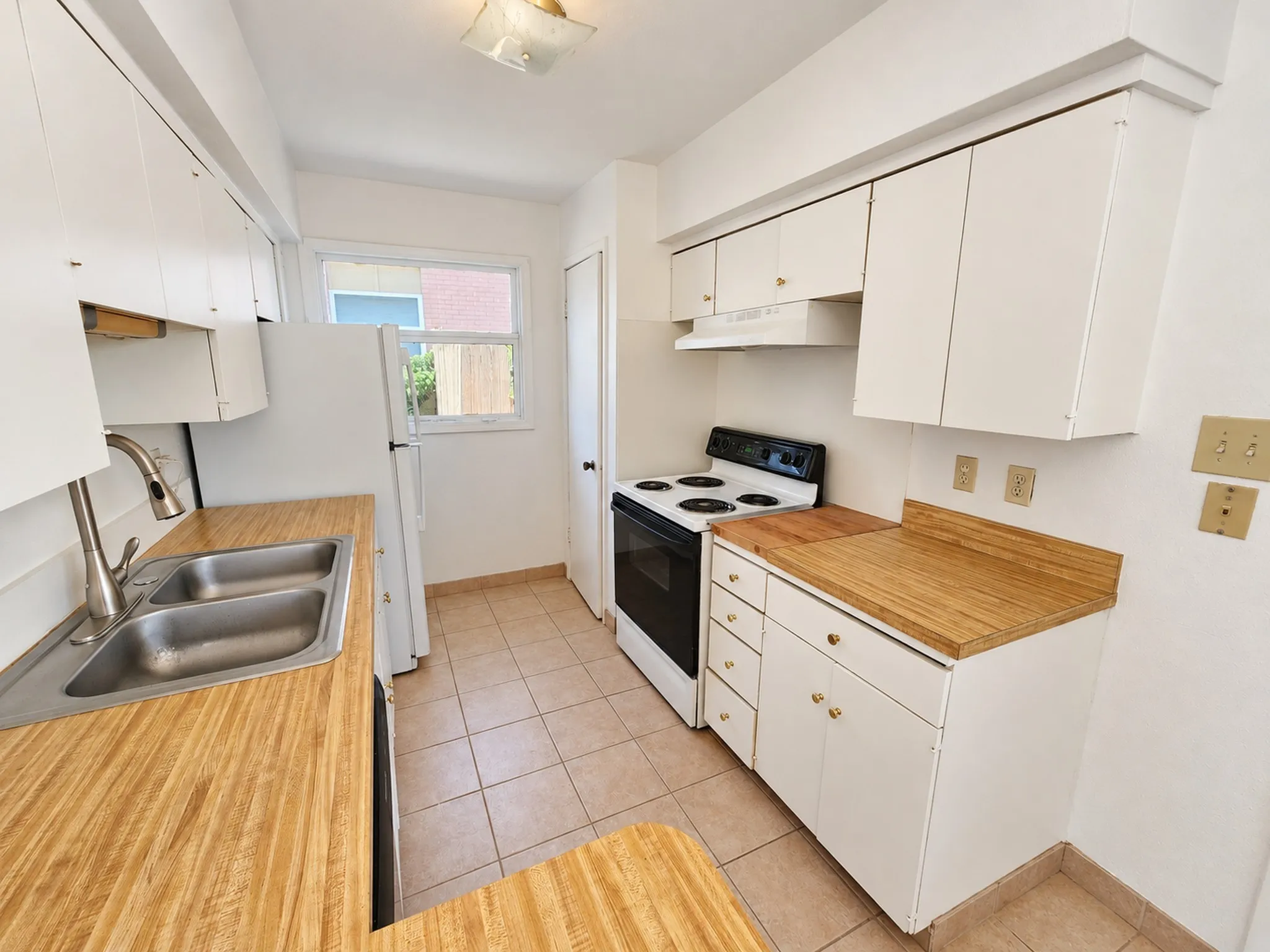 Kitchen featuring a dual basin sink with a gooseneck faucet, light wood-finish countertops, white cabinetry, a white refrigerator, and a white oven range with a matching range hood