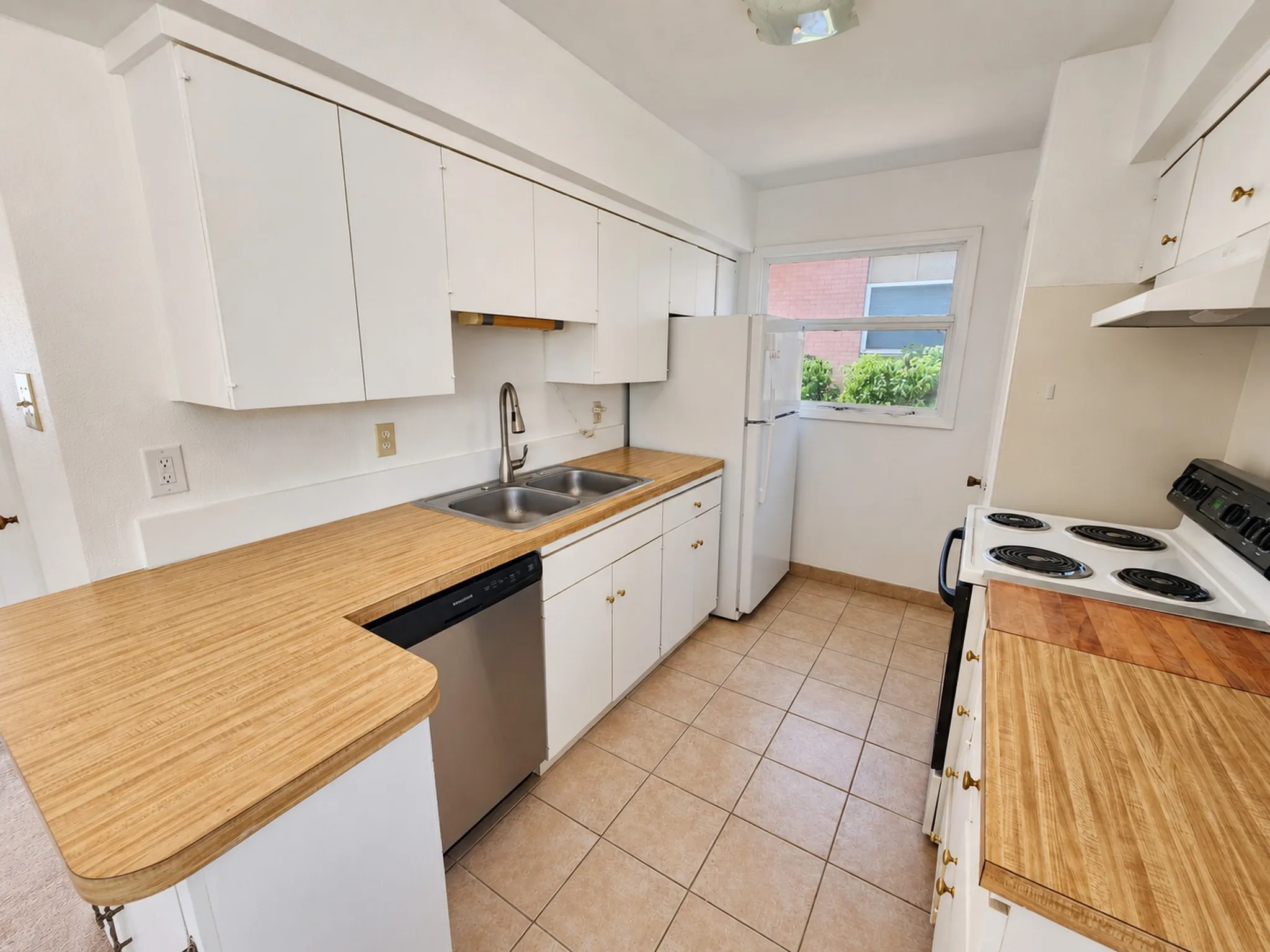 Kitchen featuring wood-finish countertops, white cabinetry, a double basin sink with a high-arc faucet, and tile flooring