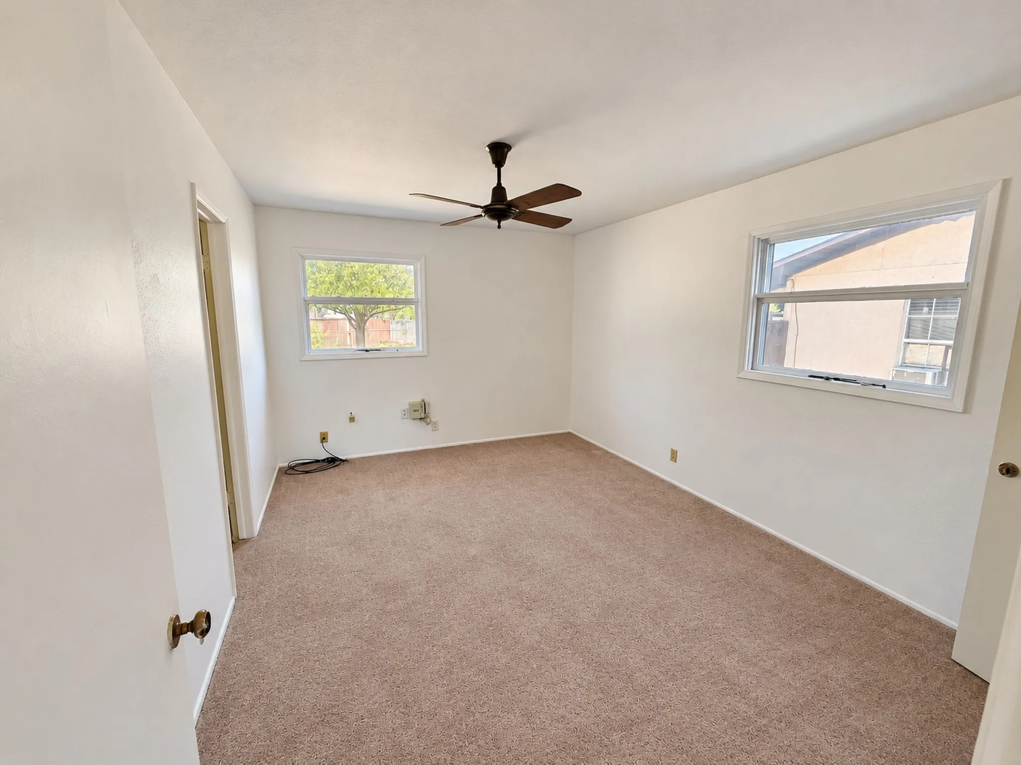 Wall-to-wall carpeting with two windows and an overhead ceiling fan