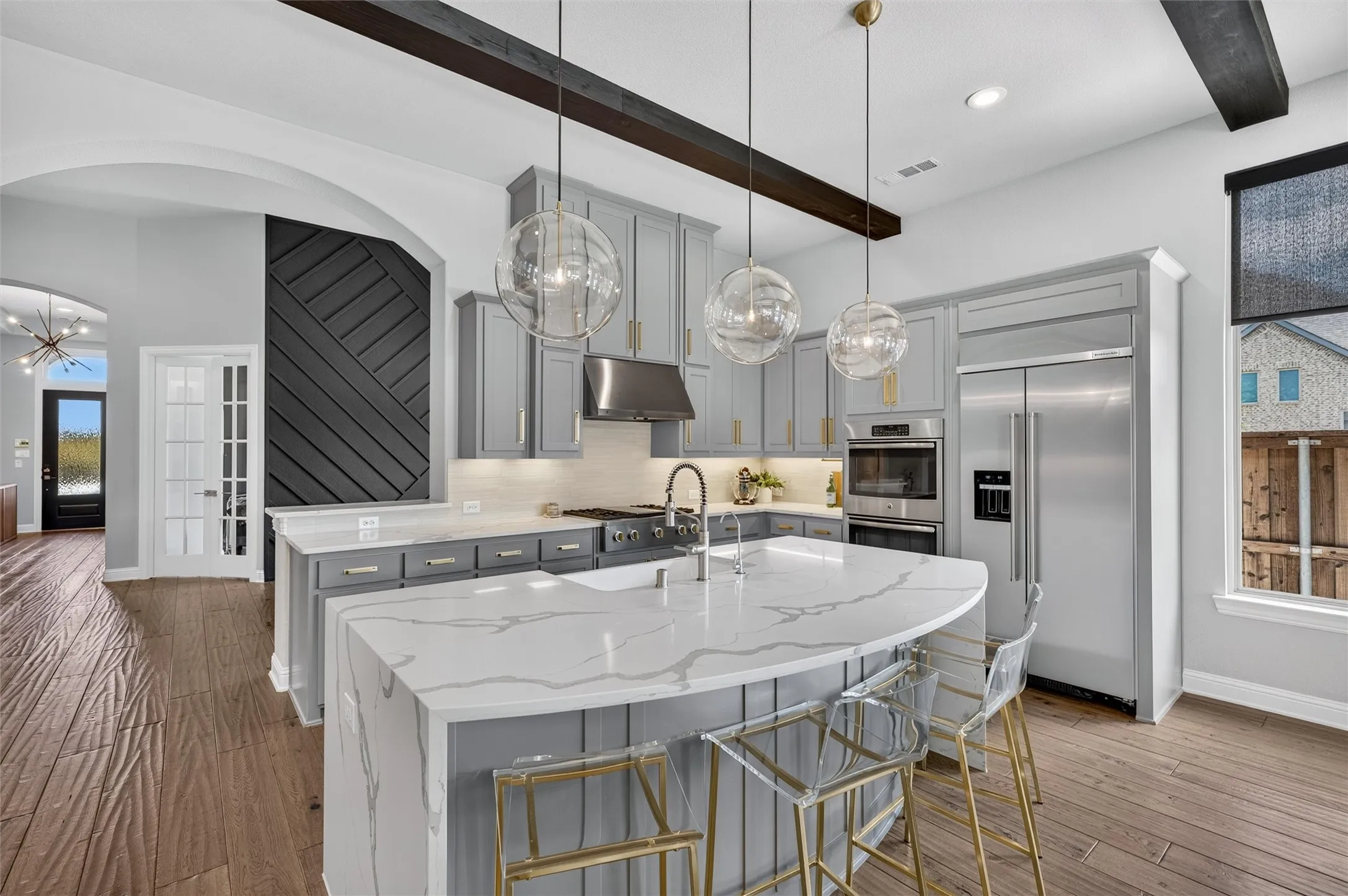 Gourmet kitchen with custom cabinetry, large kitchen island with a waterfall countertop, integrated stainless steel appliances, and wood-finish flooring