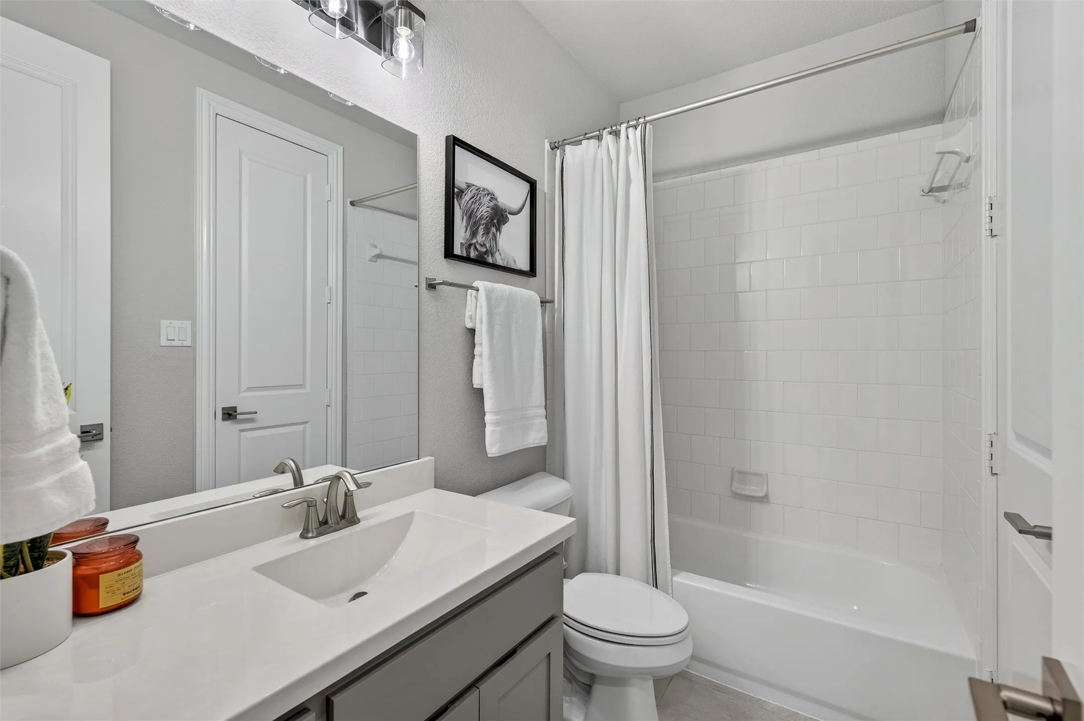 Bathroom featuring a white subway tile tub surround, a white bathtub, a single vanity with a quartz countertop, and a brushed nickel faucet