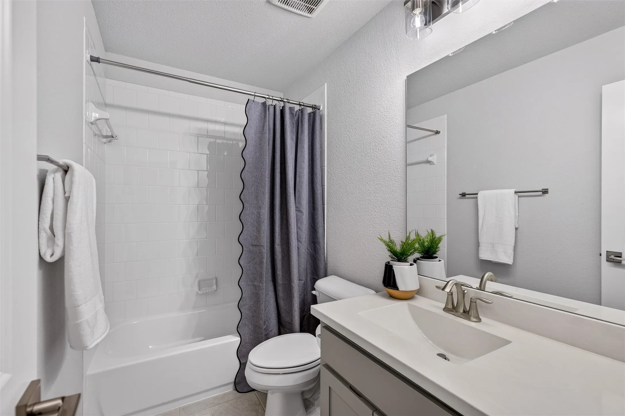 Bathroom featuring a shower-tub combination with white subway tile, a vanity with a white countertop and undermount sink, and a large wall-mounted mirror
