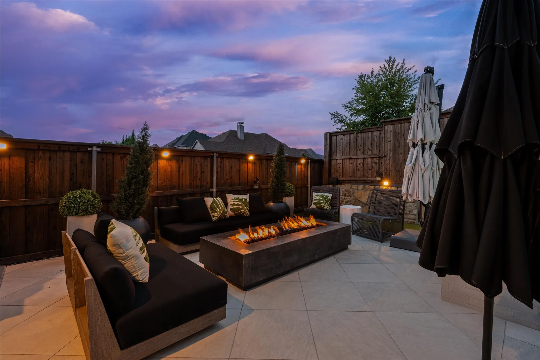 Expansive patio with large format tile flooring, a built-in fire feature, and perimeter lighting