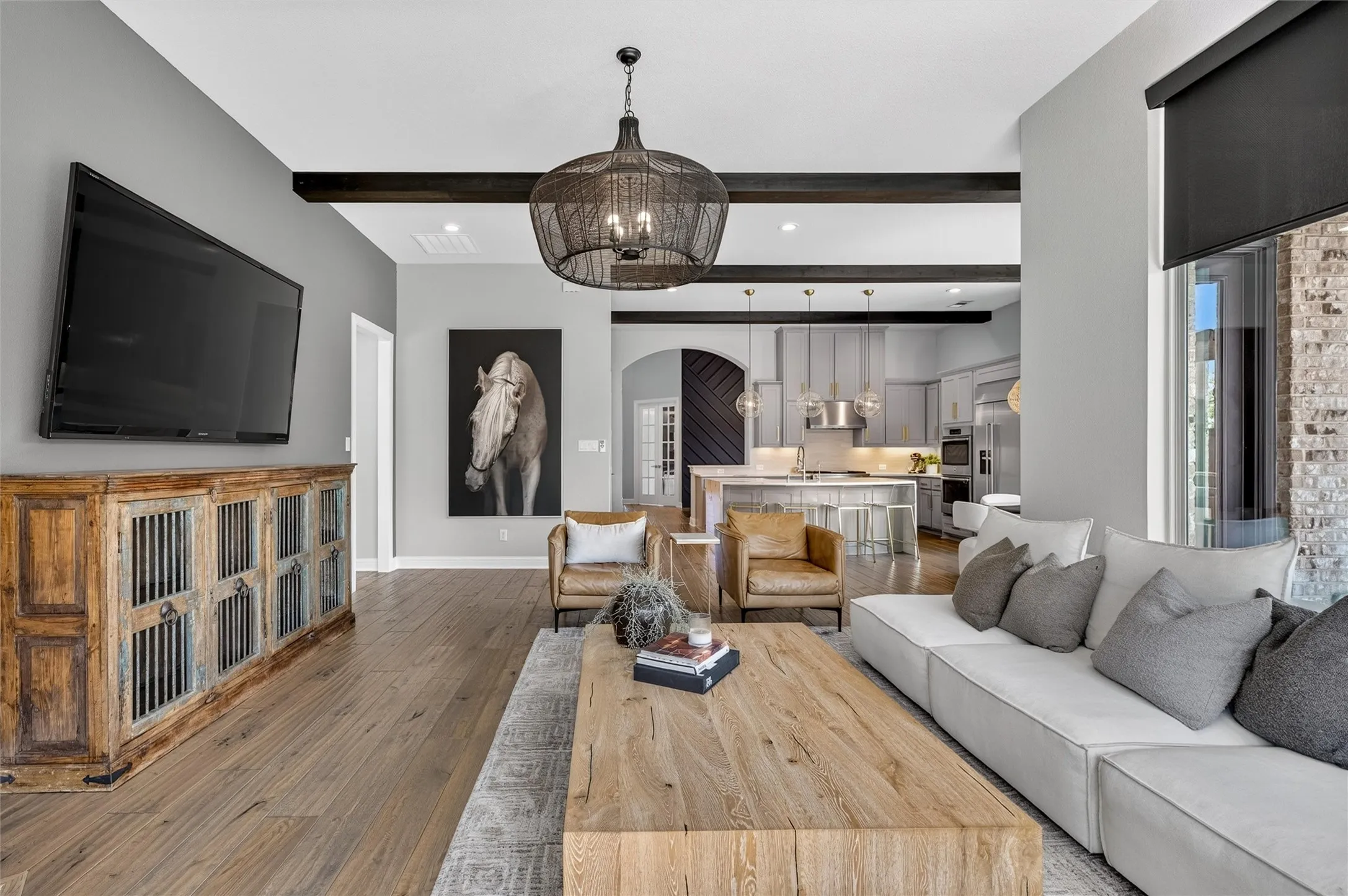 Spacious living area featuring wood-finish flooring, exposed ceiling beams, and a prominent decorative light fixture