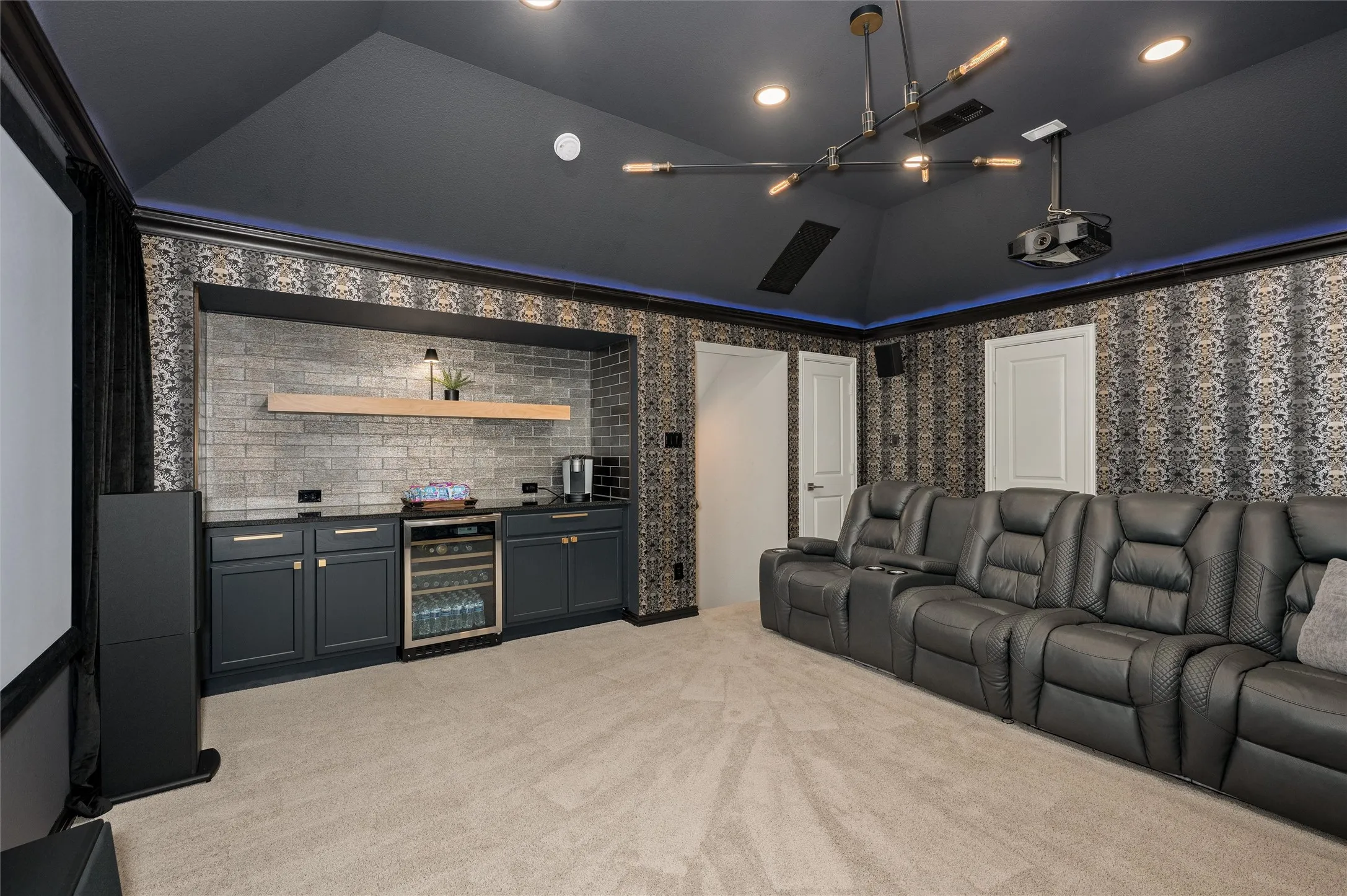 Vaulted ceiling with recessed lighting, integrated projector, built-in wet bar with beverage cooler, and accent wall with patterned wallpaper