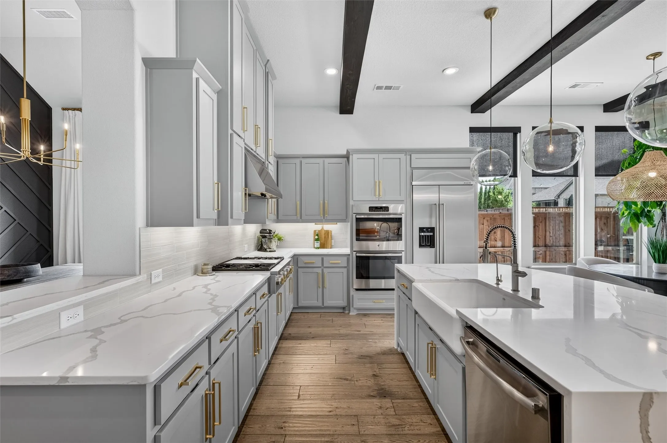 Gourmet kitchen featuring light gray cabinetry, integrated stainless steel appliances, a large center island with a farmhouse sink, under-cabinet lighting, and wood-finish flooring