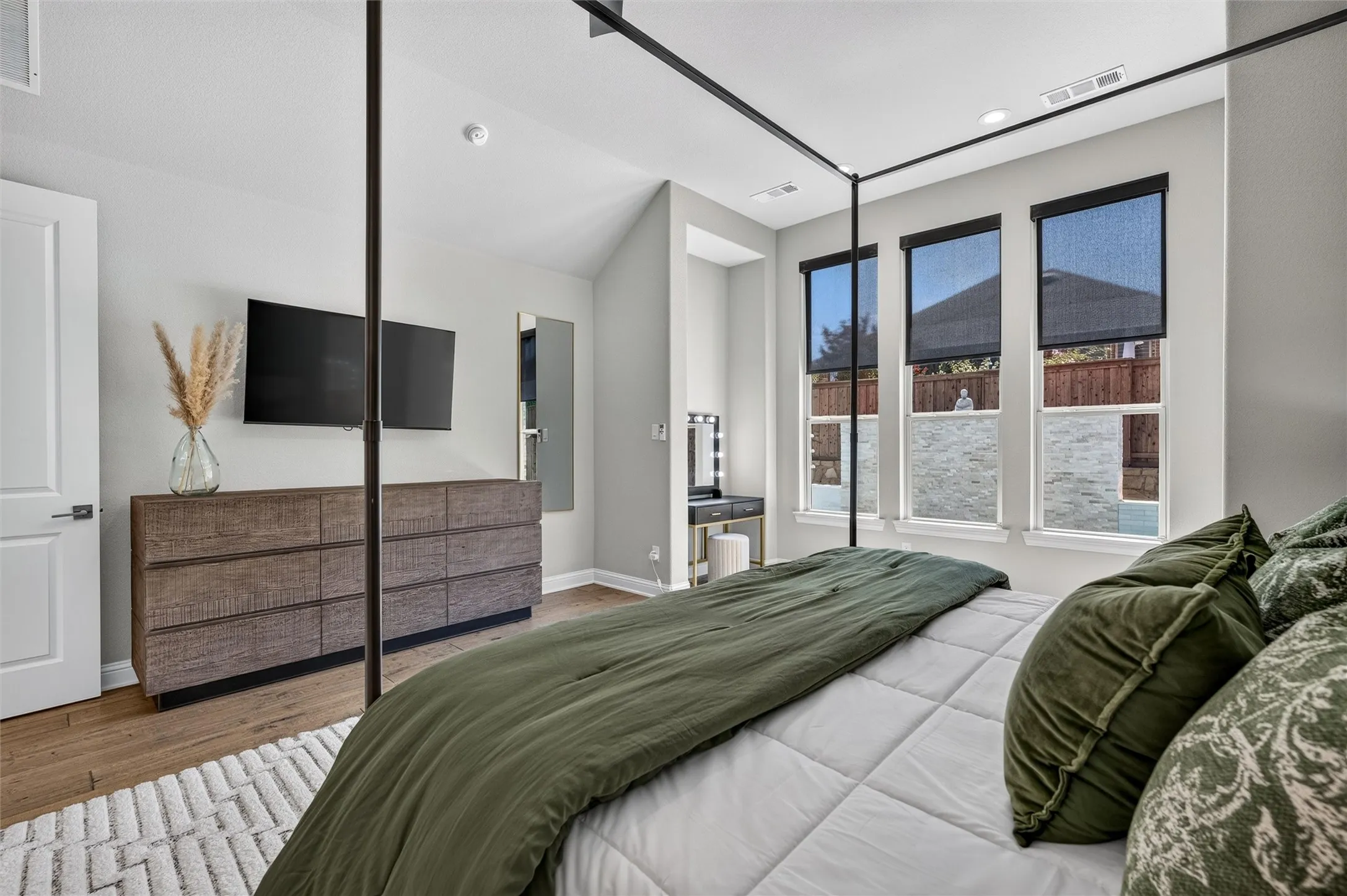 Vaulted ceiling, wood-finish flooring, white paneled door, recessed lighting, and multiple windows with roller shades