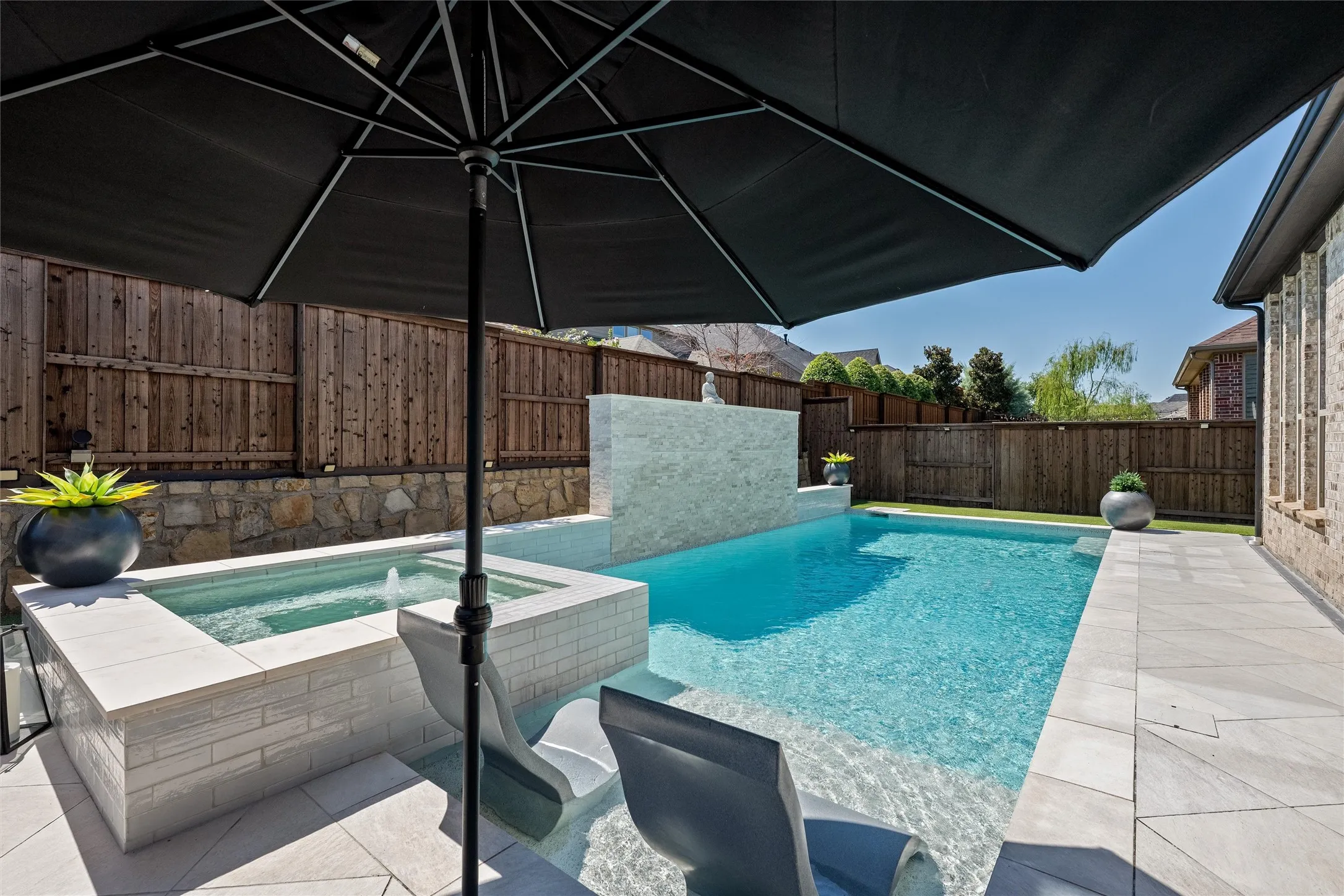 In-ground pool featuring a spillover spa, a stone accent wall, and perimeter paving