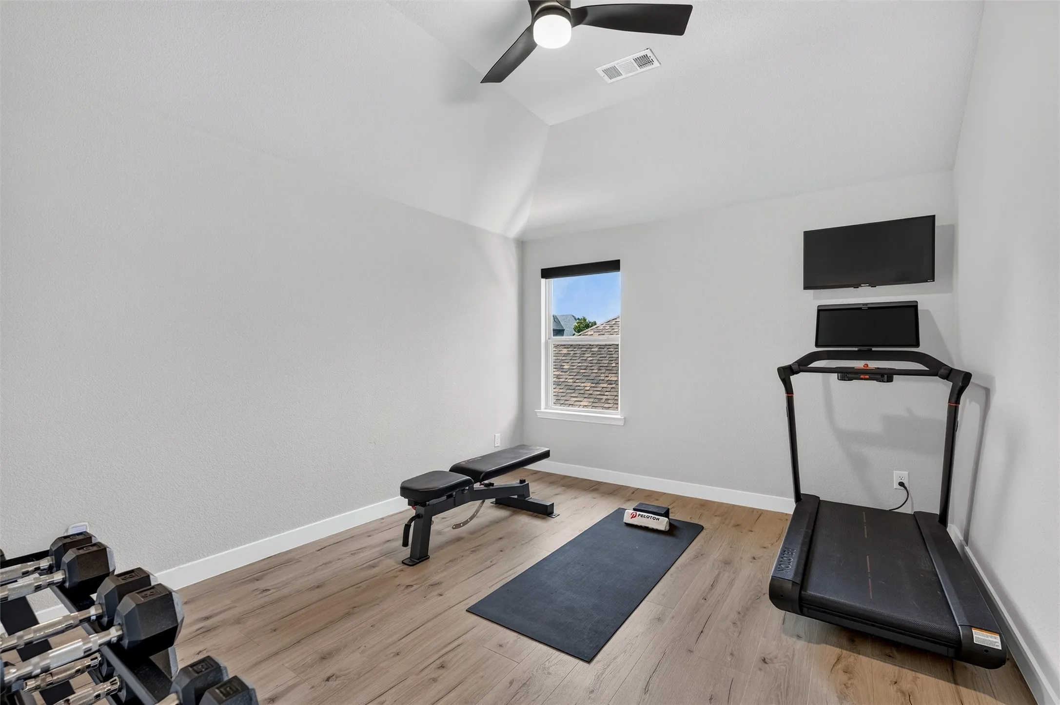 Vaulted ceiling, wood-finish flooring, ceiling fan, and a window with a stone exterior