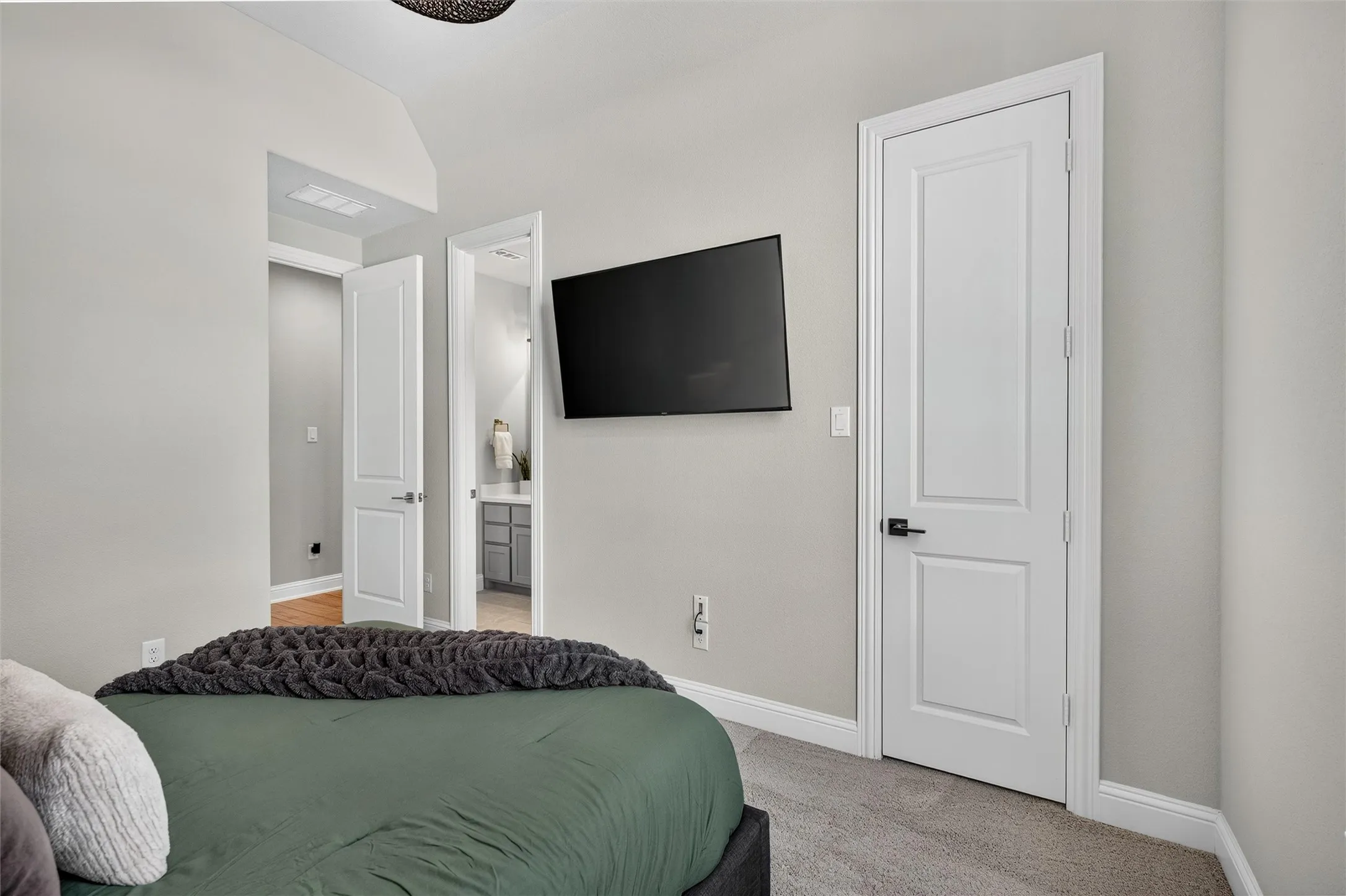 Wall-mounted television fixture, light gray wall color, white paneled doors, black door hardware, and light gray carpeting