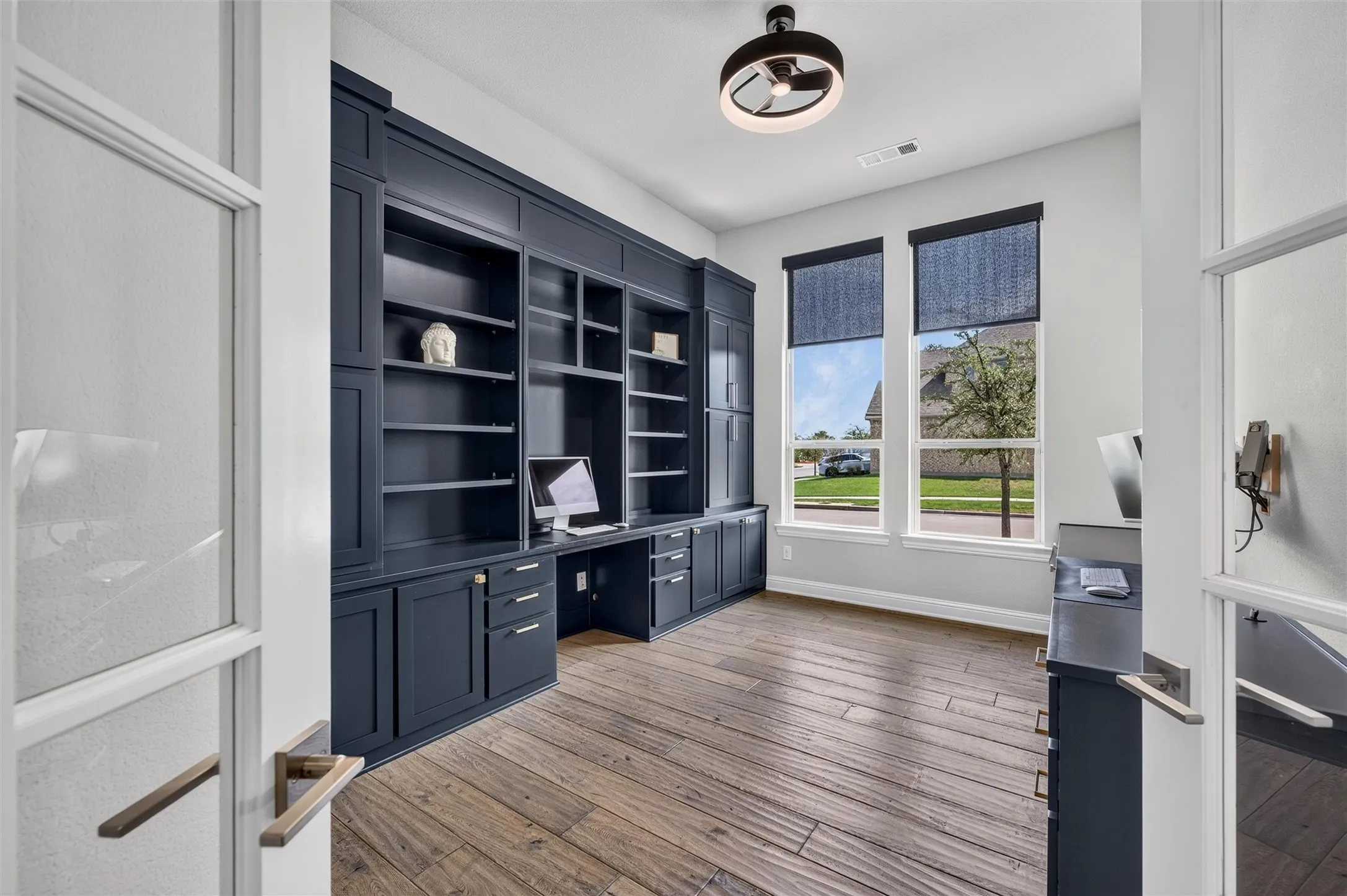 Wood-finish flooring, built-in dark cabinetry with integrated desk space, dual windows with roller shades, and a modern ceiling fixture