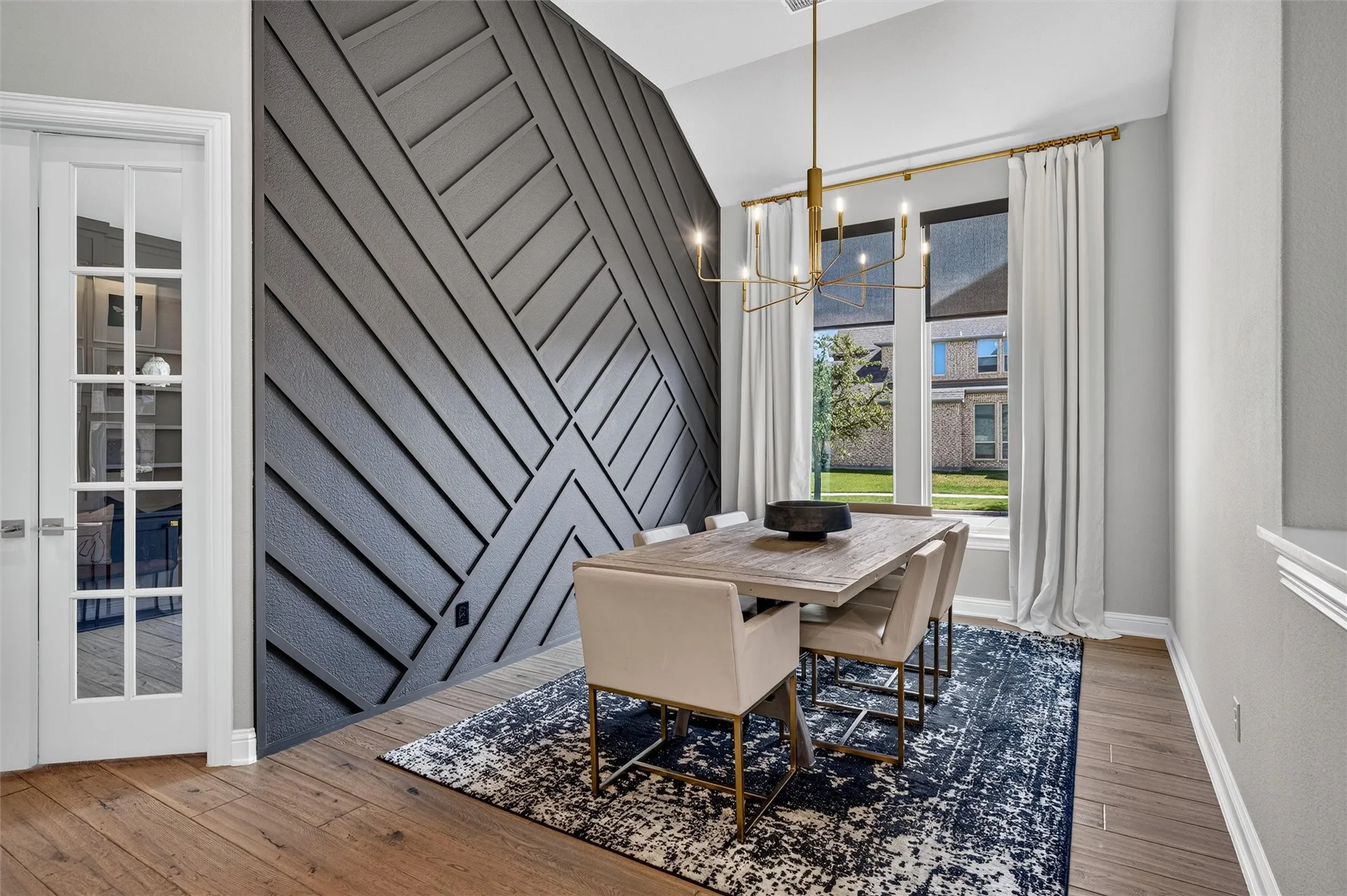 Herringbone accent wall, wood-finish flooring, vaulted ceiling, multi-pane French doors, and a contemporary chandelier