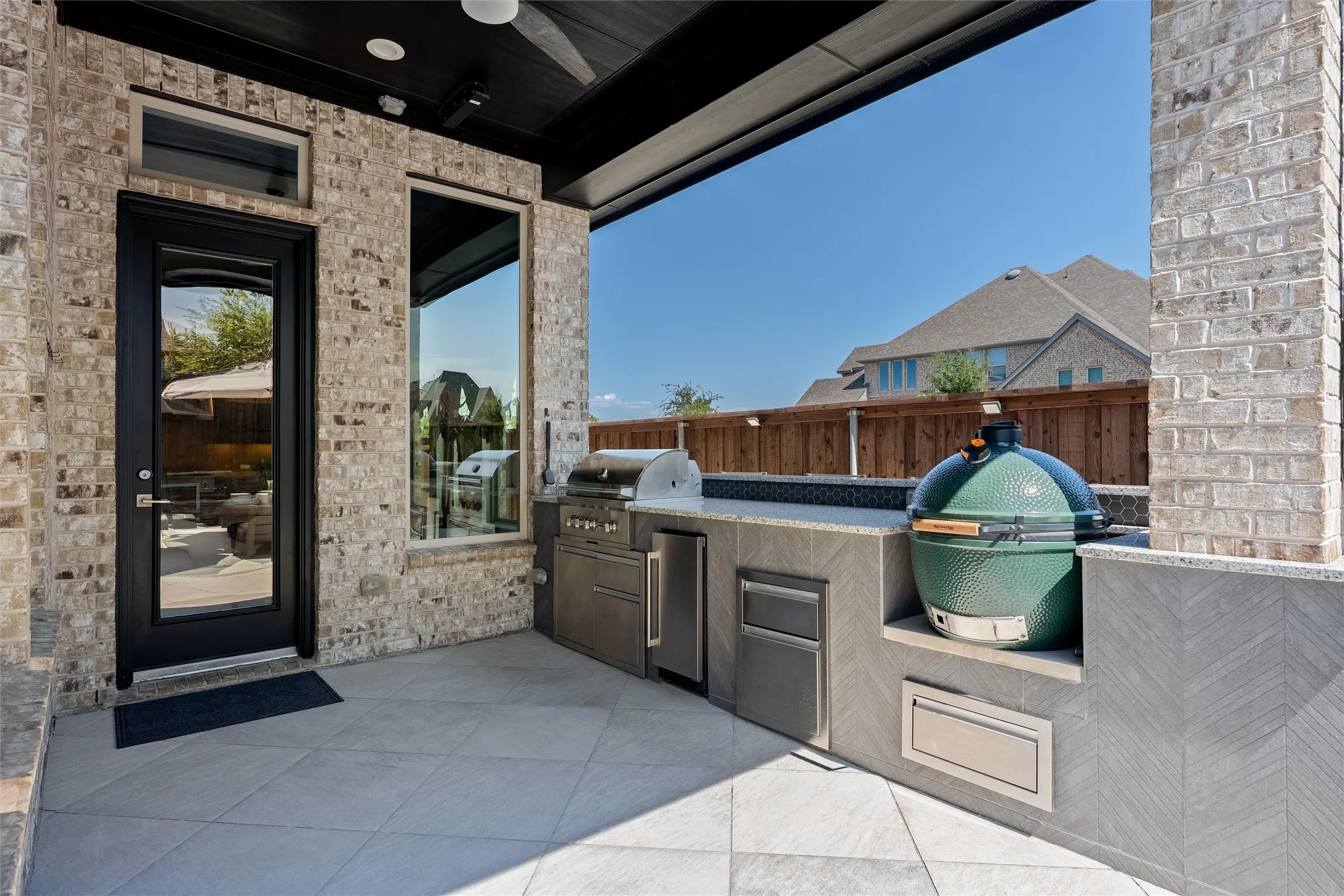 Covered outdoor patio featuring brick exterior, built-in outdoor kitchen with grill, integrated outdoor cooking appliance, and light-toned tile flooring