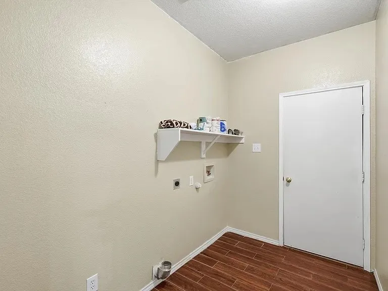 Dedicated utility room featuring wood-finish flooring, light-colored walls, a white wall-mounted shelf, and a white door with a brass-finish knob