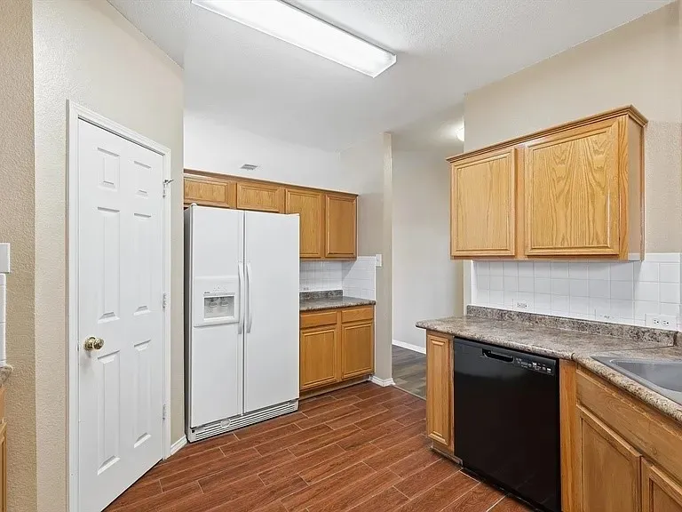 Kitchen featuring wood-finish flooring, natural wood cabinetry, laminate countertops, a white tile backsplash, and a black dishwasher
