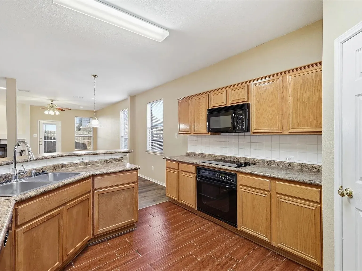 Kitchen featuring wood-finish cabinetry, granite-style countertops, an undermount double basin stainless steel sink, black built-in appliances, and tile flooring