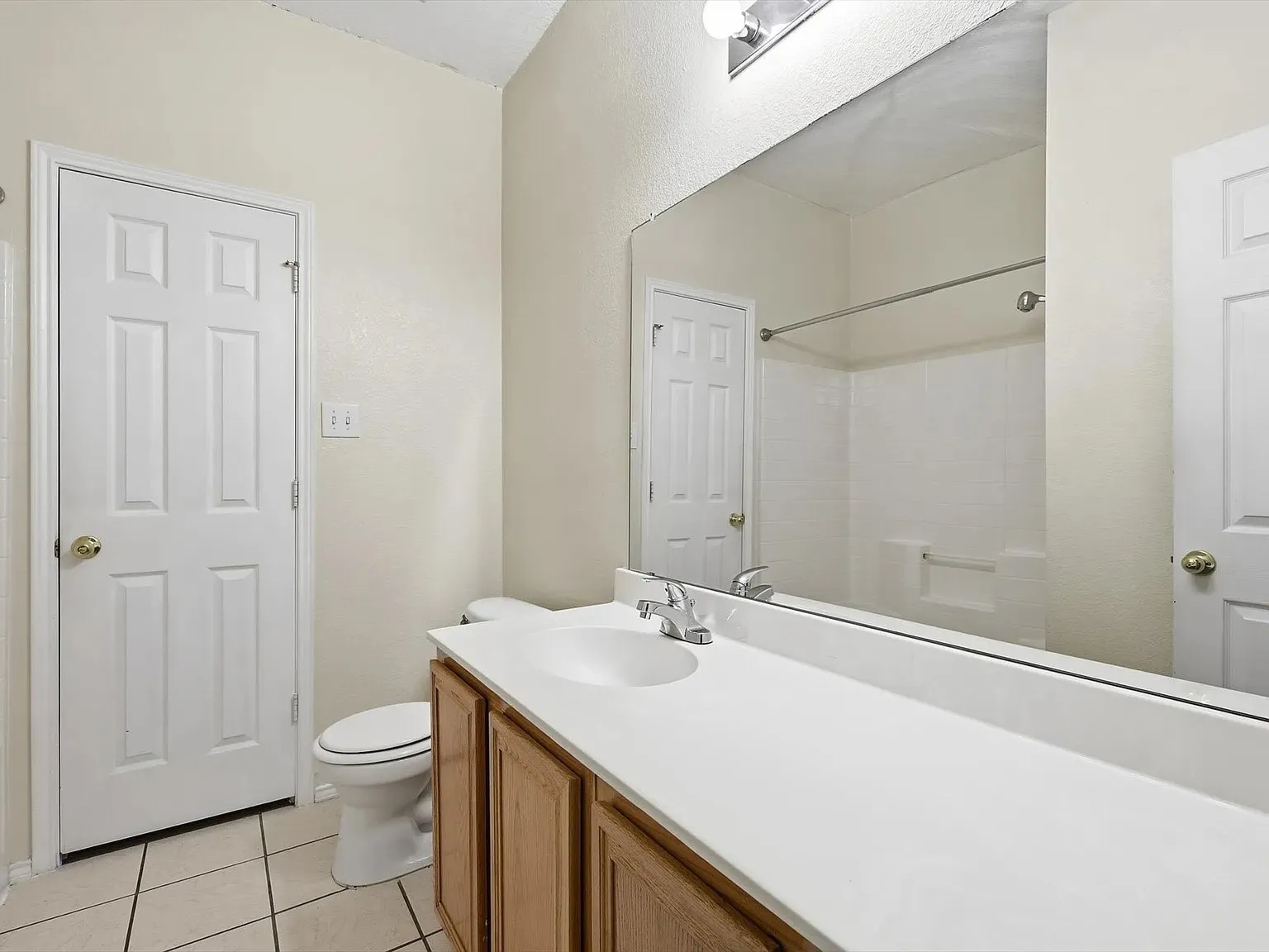 Bathroom vanity featuring a single basin sink set into a white countertop, with wood-finish cabinetry below
