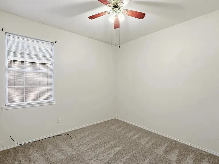 Neutral tone wall paint, textured carpet flooring, window with blinds, and a ceiling fan with integrated lighting