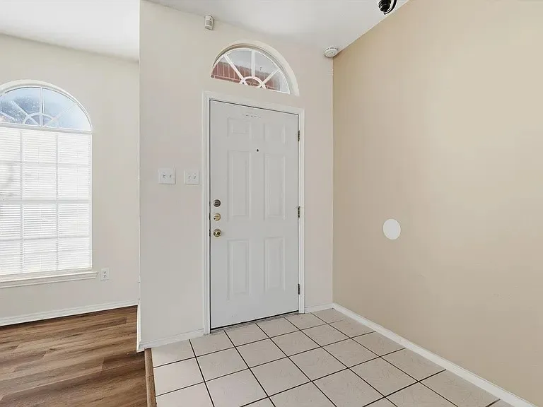 Entryway featuring a paneled door with an arched transom, a large arched window with blinds, tile flooring, and wood-finish flooring