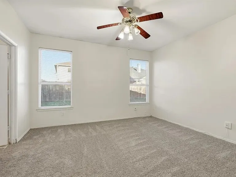 Spacious carpeted room featuring a ceiling fan with integrated lighting, two windows with blinds, and neutral wall tones