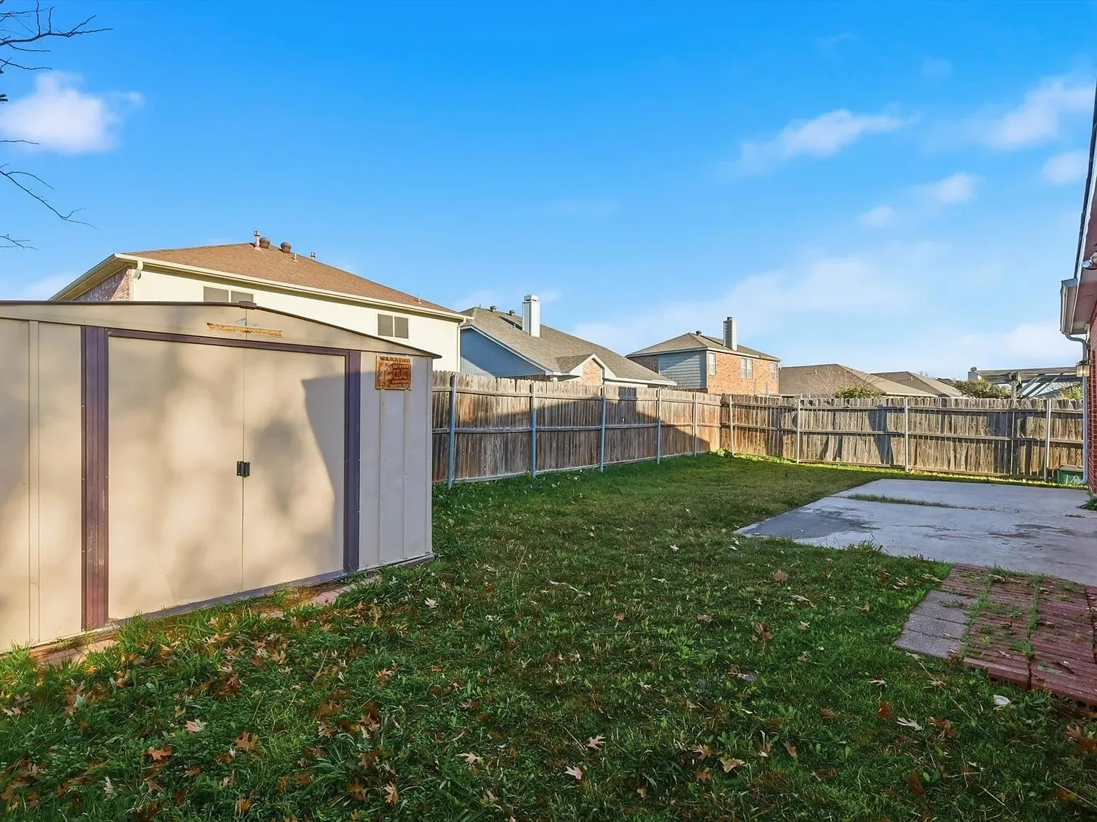 Expansive backyard featuring a lush lawn, concrete patio, and a storage shed