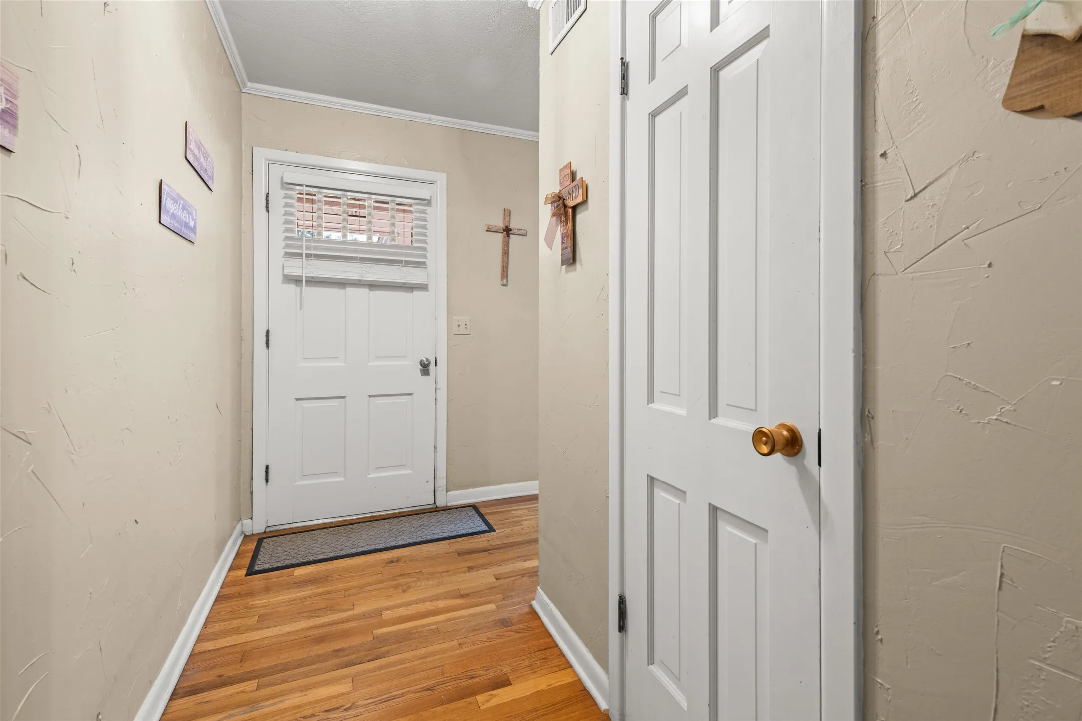 Hardwood flooring, painted interior door, textured wall finish, crown molding, and a paneled white door