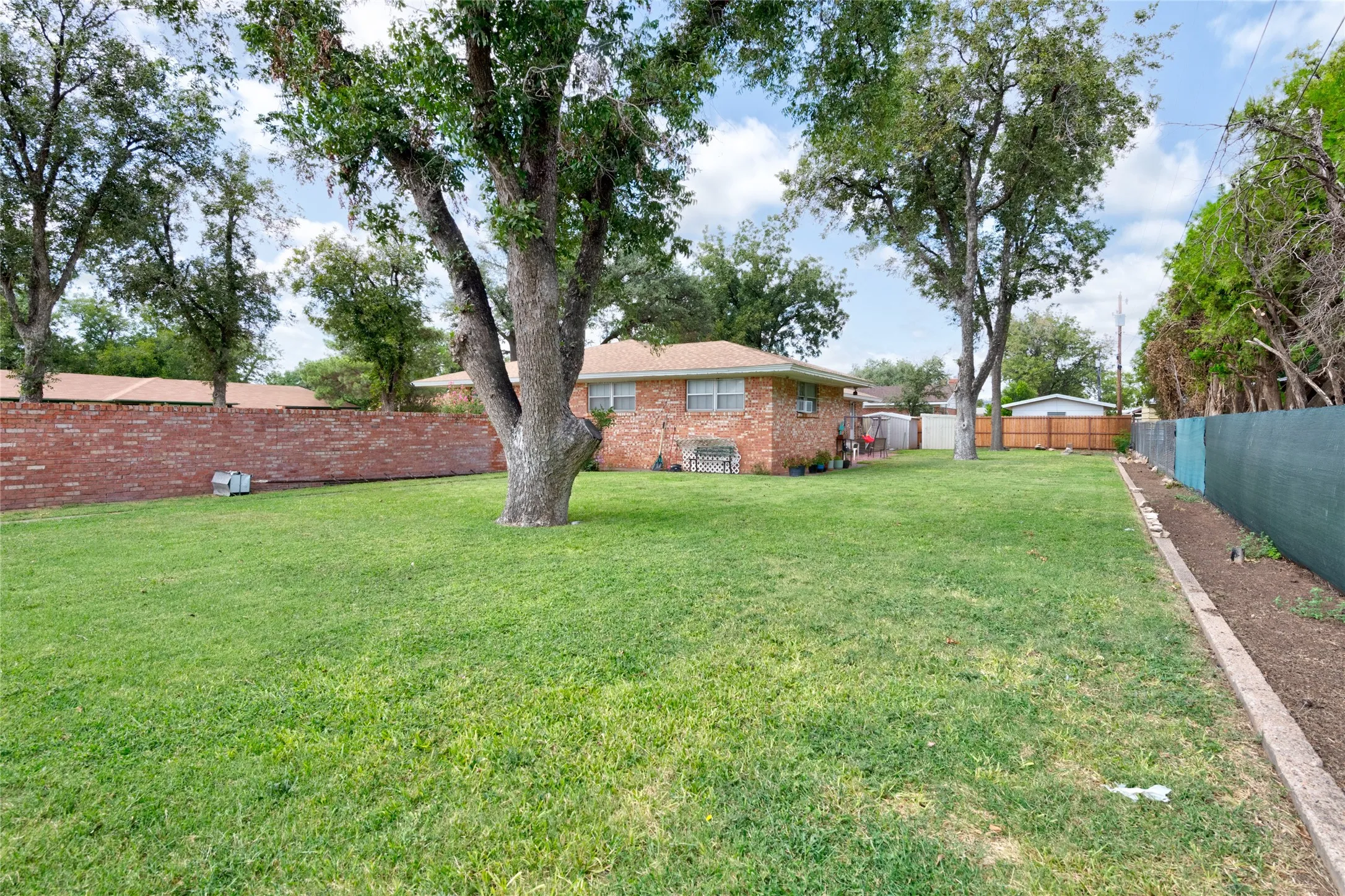 Expansive backyard featuring a large mature tree, brick exterior, and a privacy fence