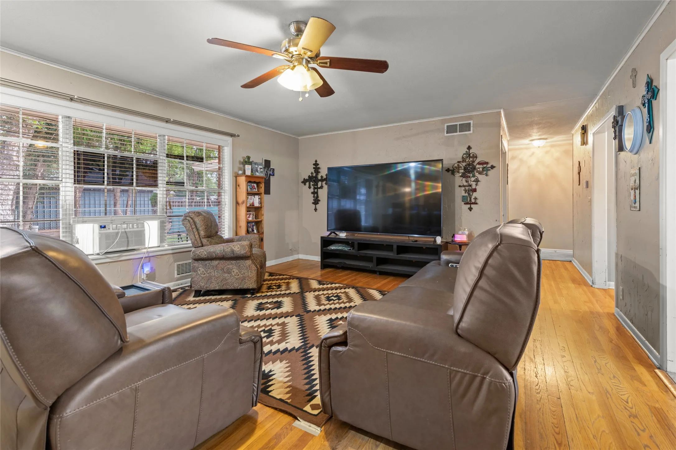 Hardwood flooring throughout, large windows with blinds, ceiling fan, and wall-mounted lighting fixtures