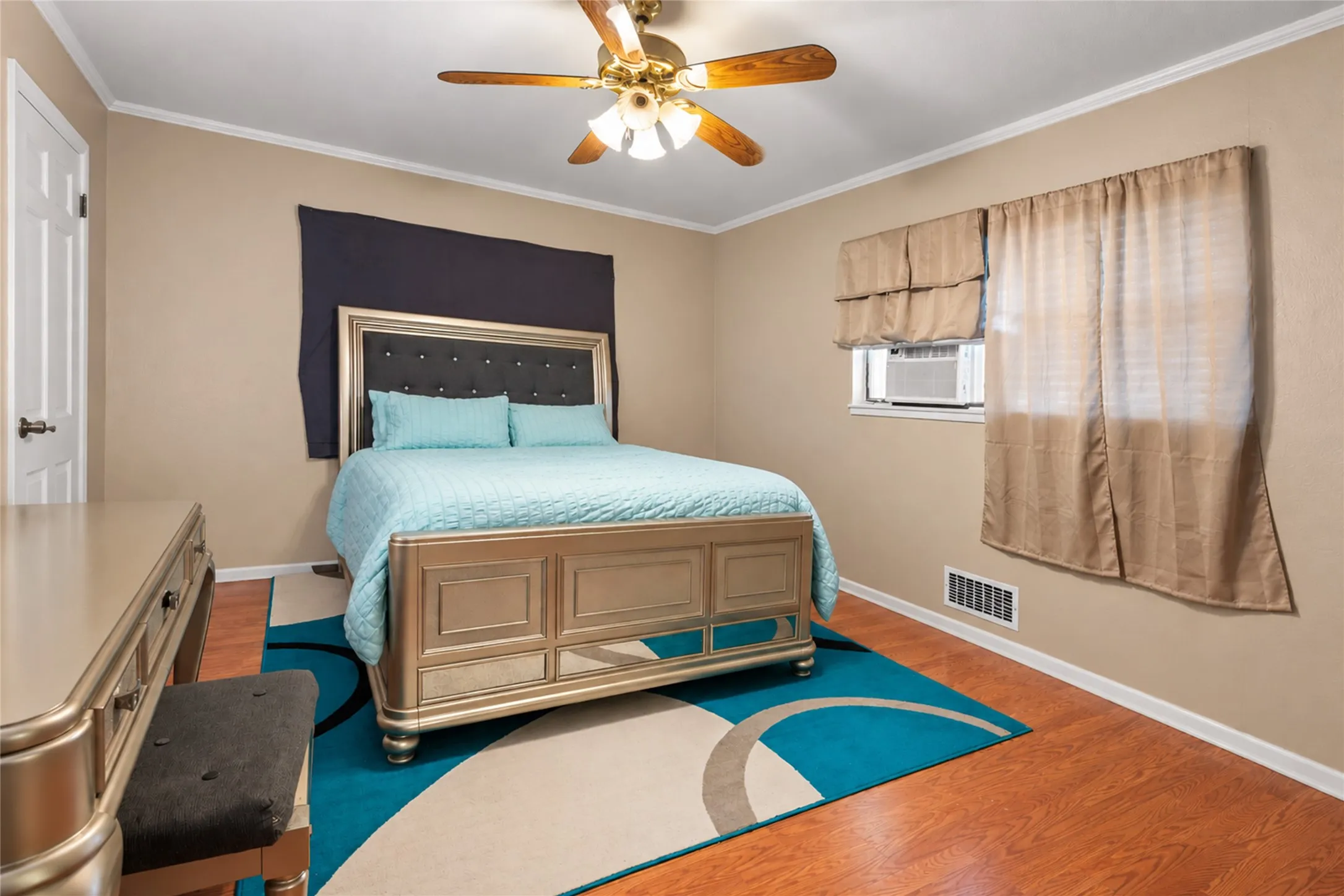 Wood-finish flooring with crisp white baseboards, crown molding, and a ceiling fan with integrated lighting