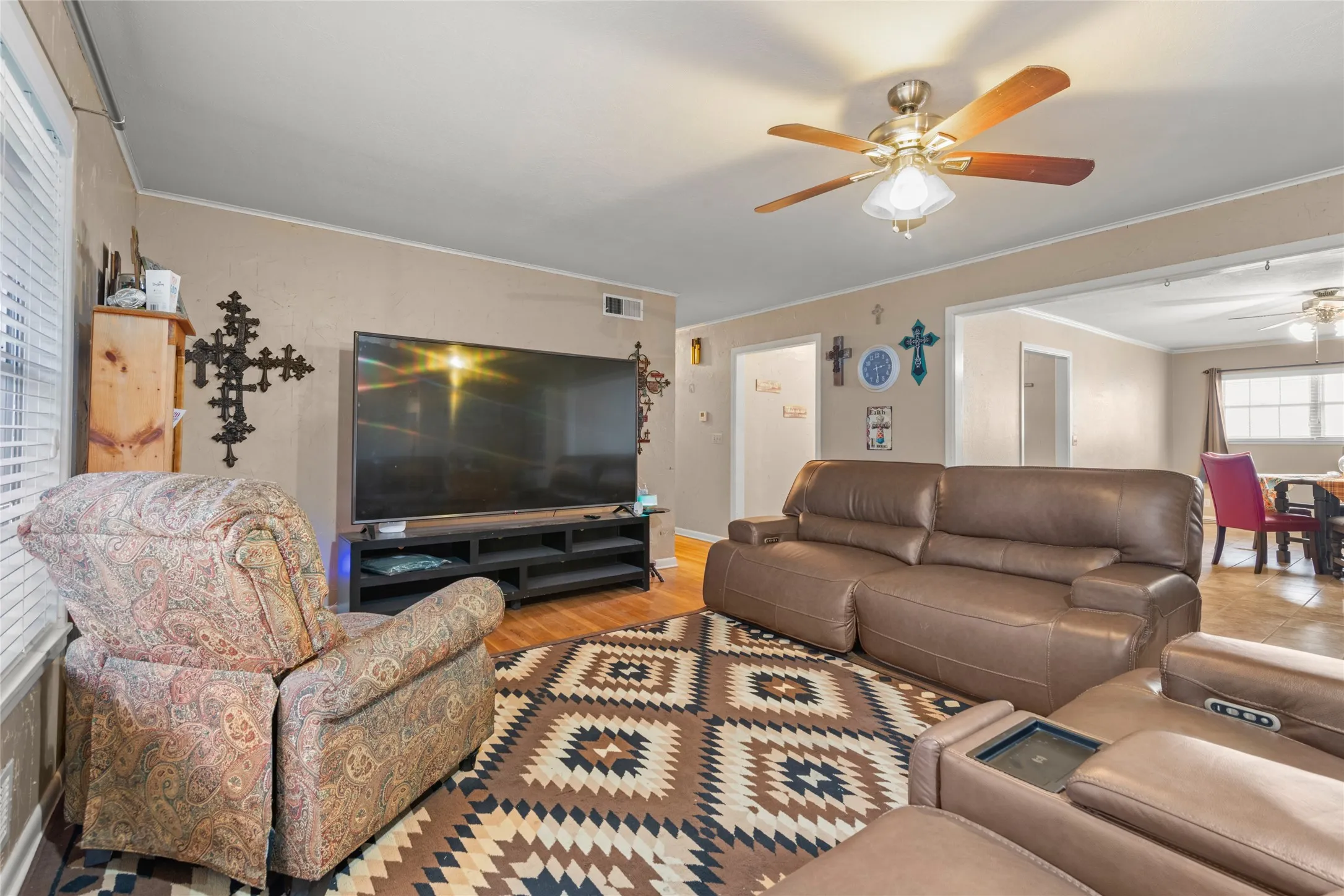 Wood-finish flooring throughout, ceiling fan with integrated lighting, and a large open doorway to an additional room