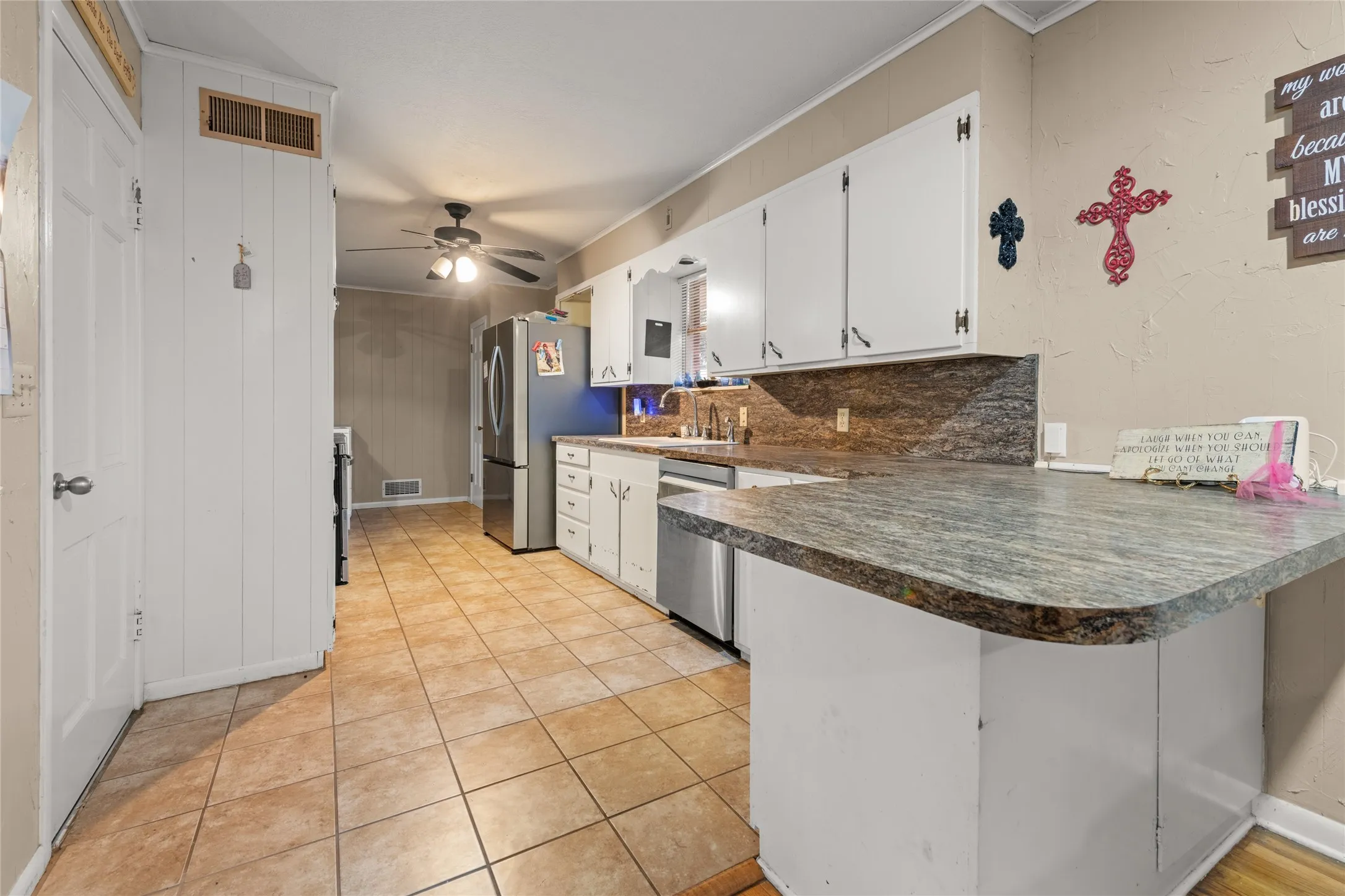Kitchen featuring a peninsula with a stone-finish countertop, white cabinetry, tile flooring, and stainless steel appliances