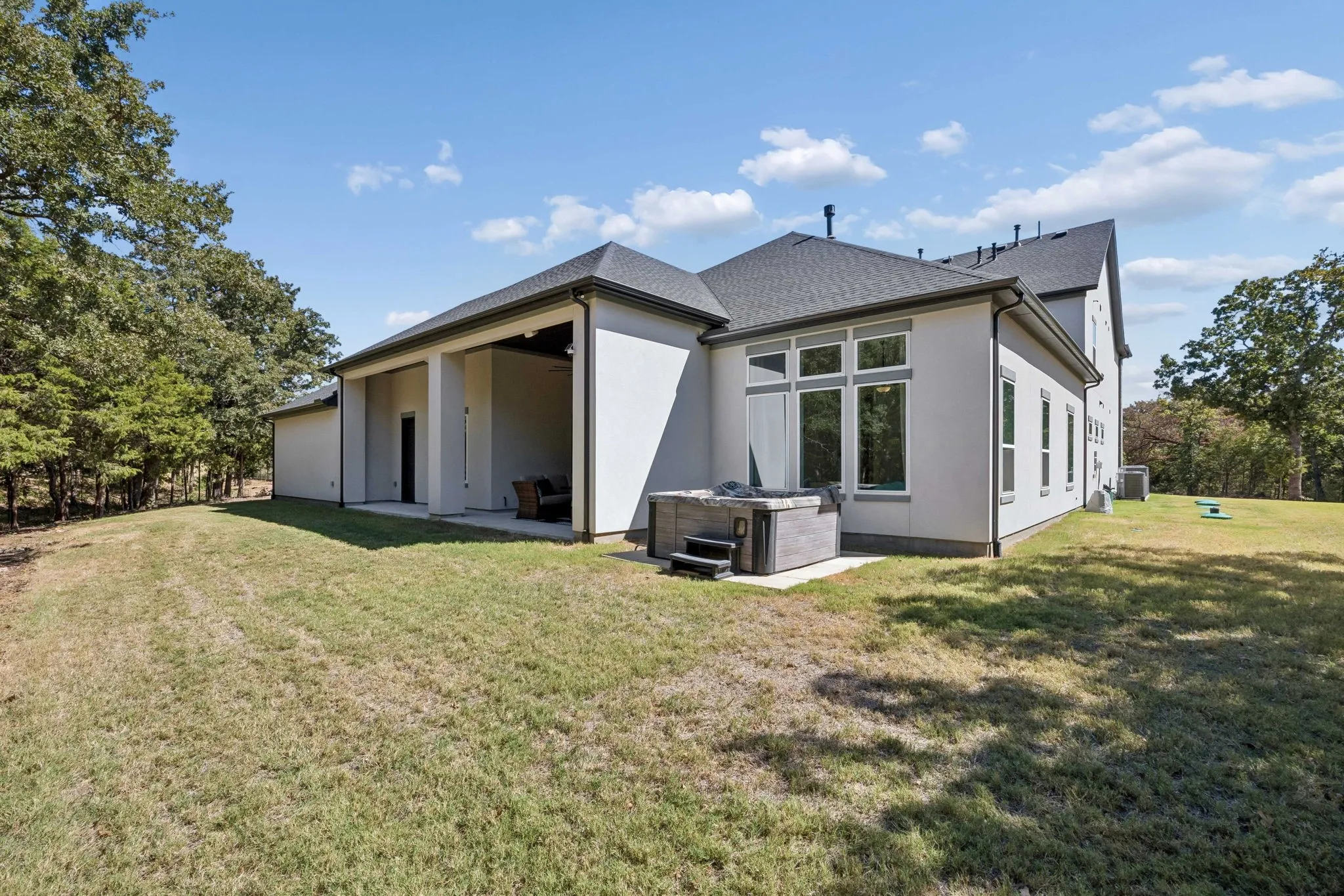 Expansive backyard with a covered patio, built-in hot tub, and multiple large windows
