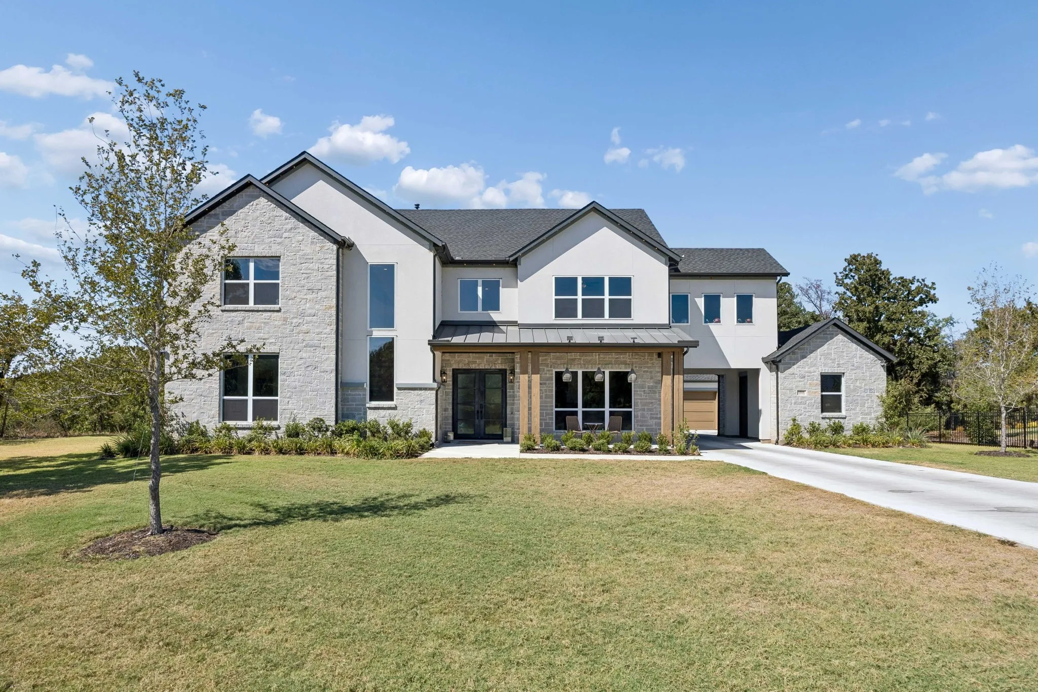 Contemporary residence featuring a stone and stucco exterior, dark shingle roof, and a wood-accented covered entry